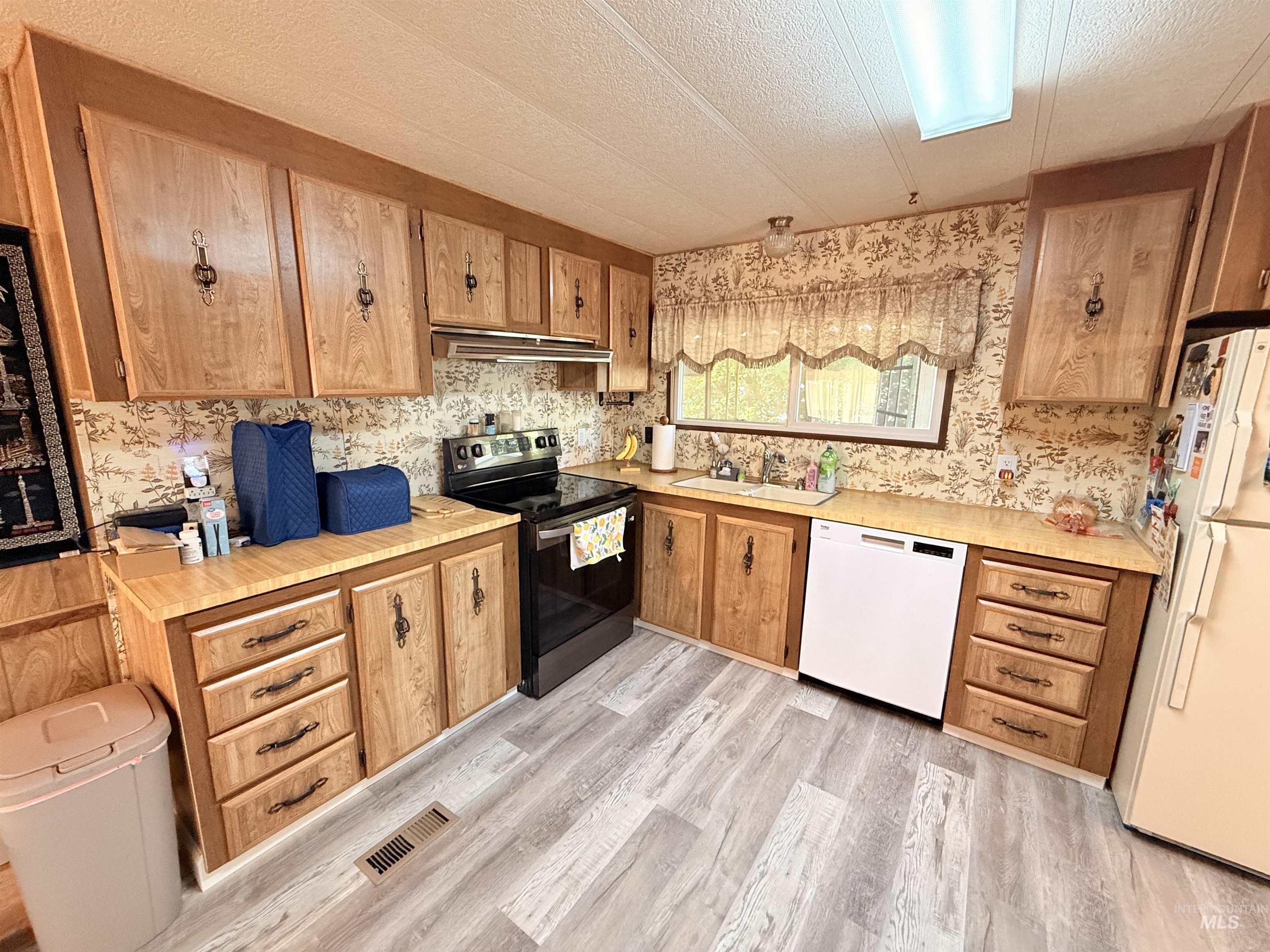 Kitchen with white appliances, a textured ceiling, light countertops, light wood-style flooring, and under cabinet range hood