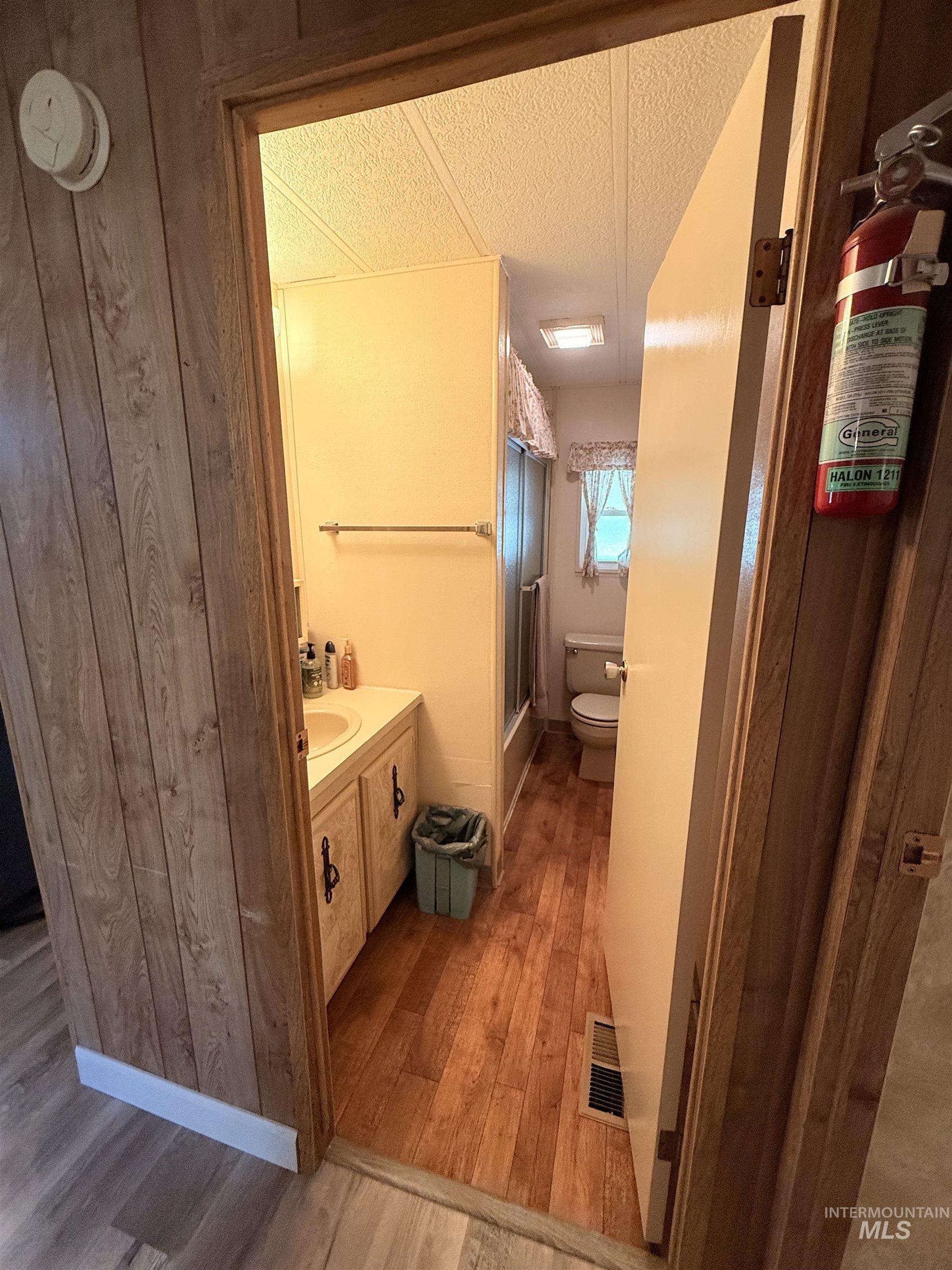 Bathroom with vanity, light wood-style floors, bath / shower combo with glass door, and a textured ceiling