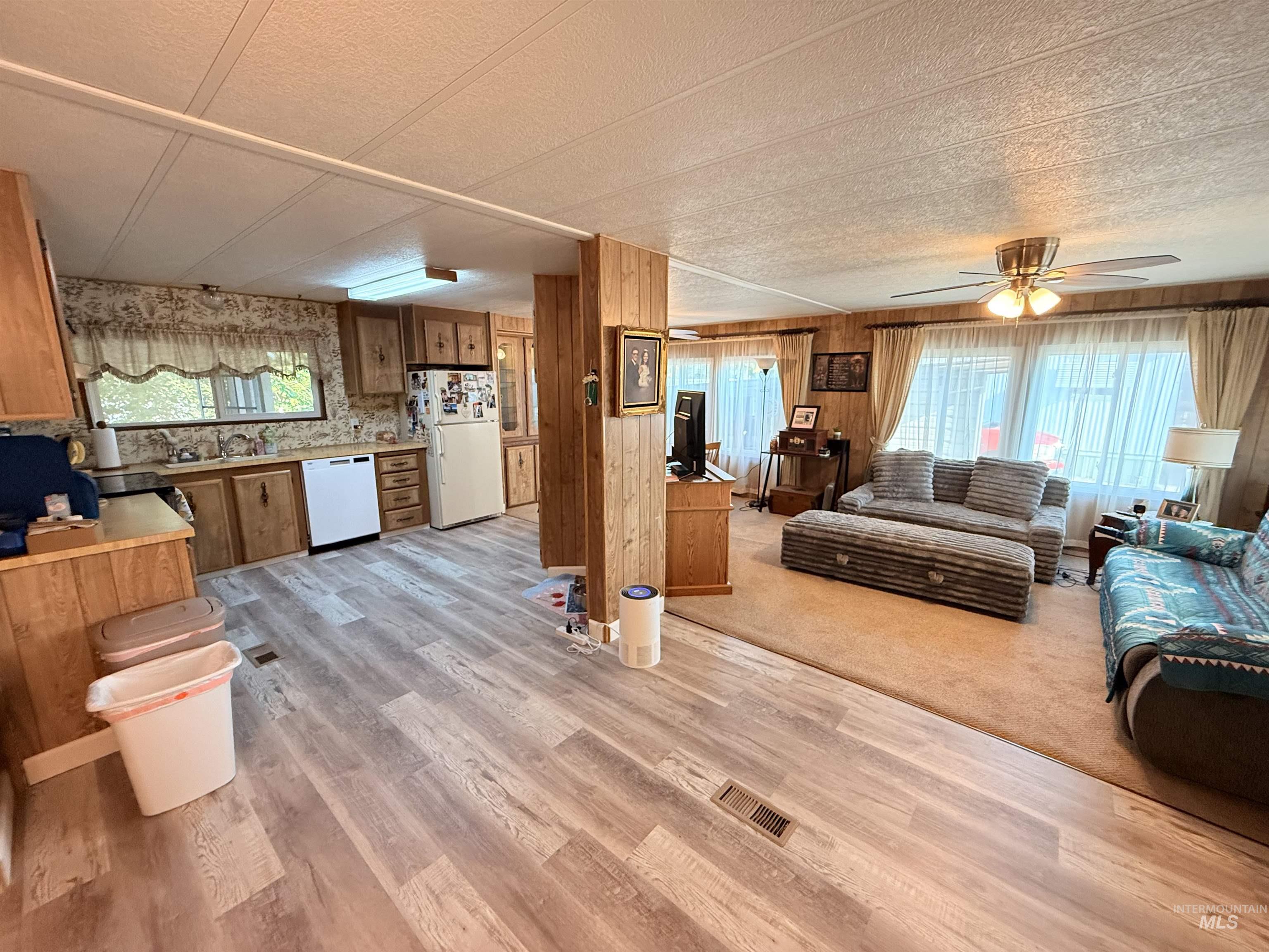 Living area with healthy amount of natural light, light wood-type flooring, wooden walls, a textured ceiling, and ceiling fan