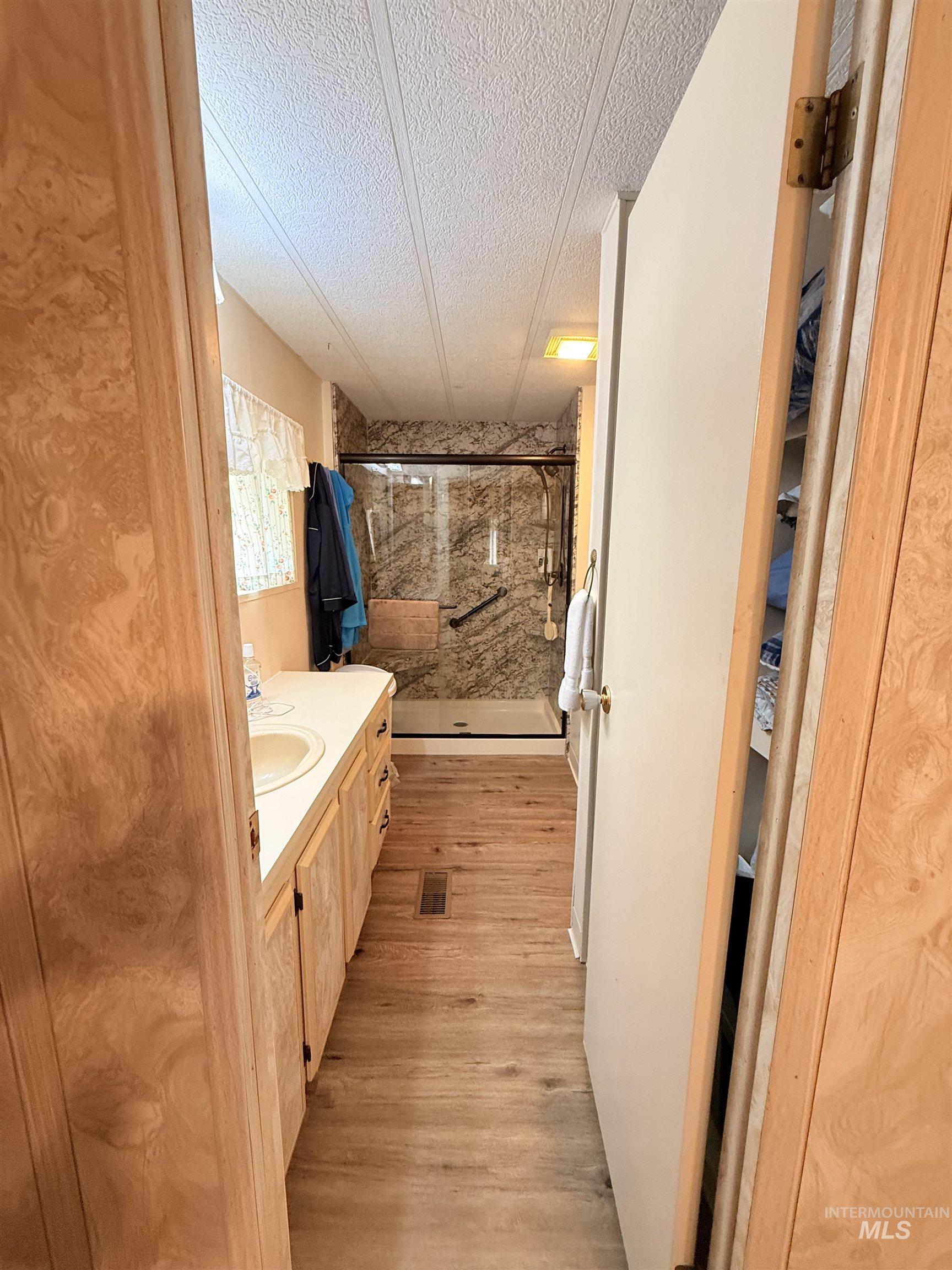 Full bathroom with a shower stall, vanity, a textured ceiling, and light wood-type flooring