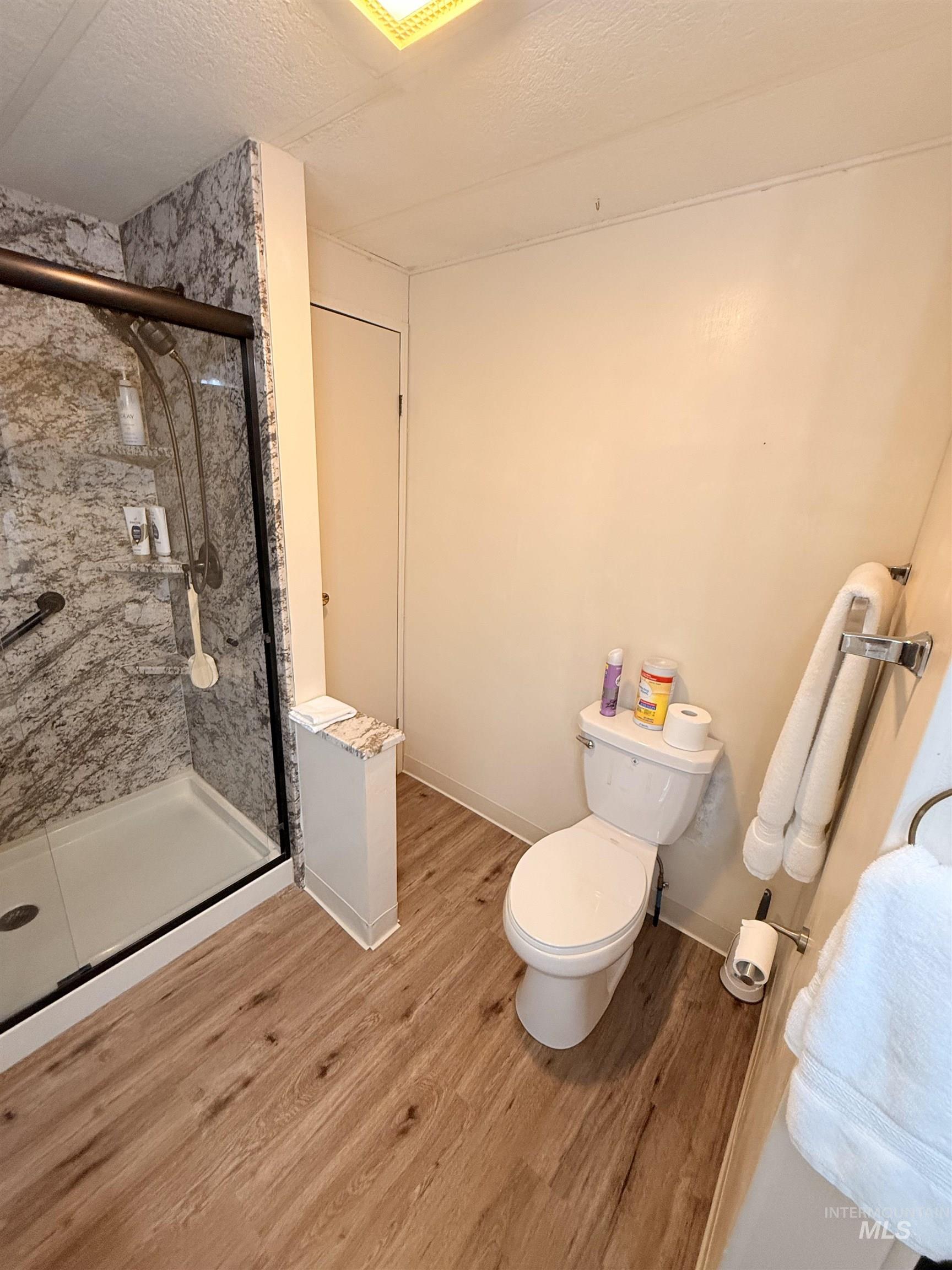 Full bathroom with light wood-style flooring, a stall shower, and a textured ceiling