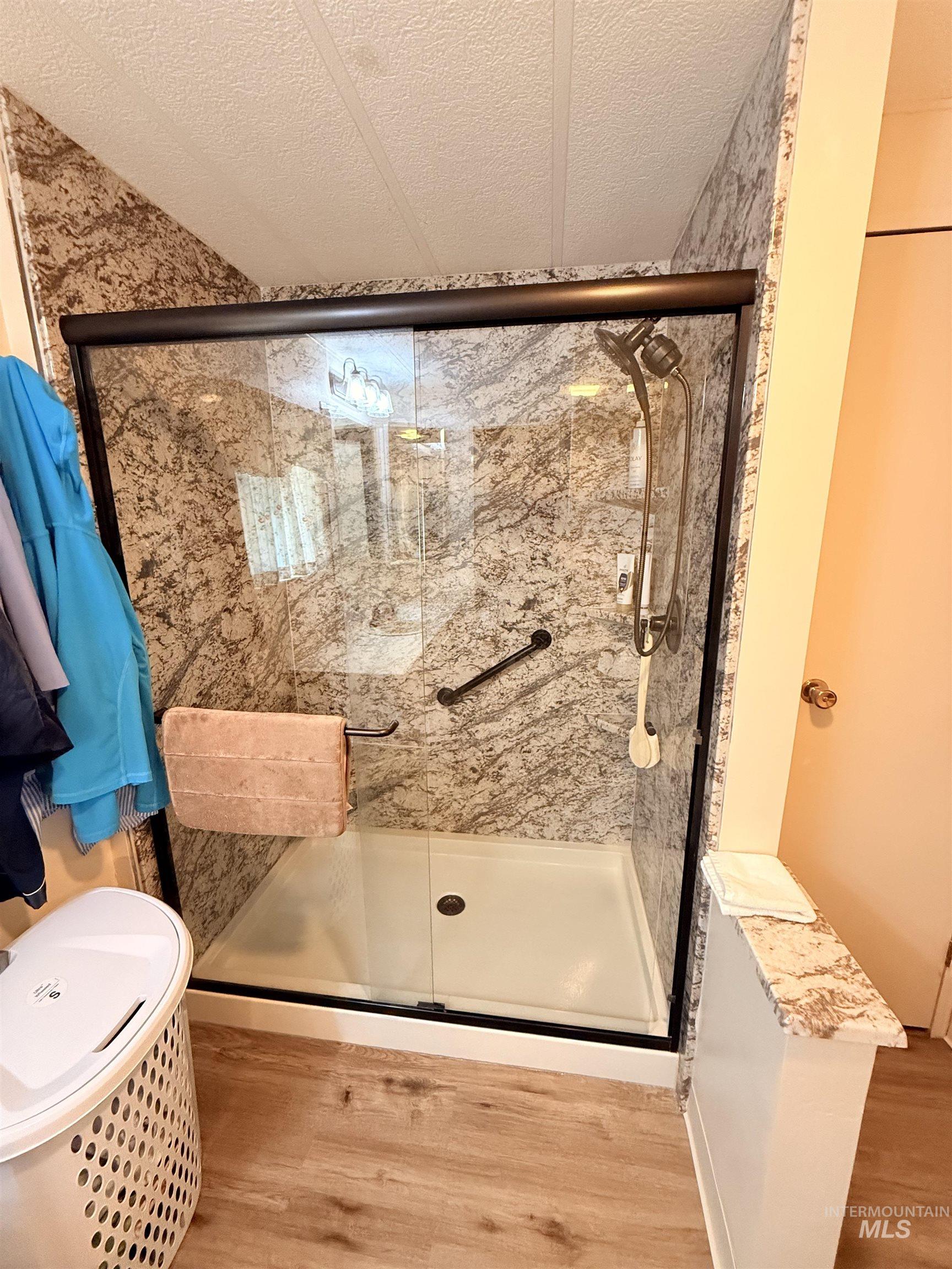 Full bath featuring wood finished floors, a stall shower, and a textured ceiling