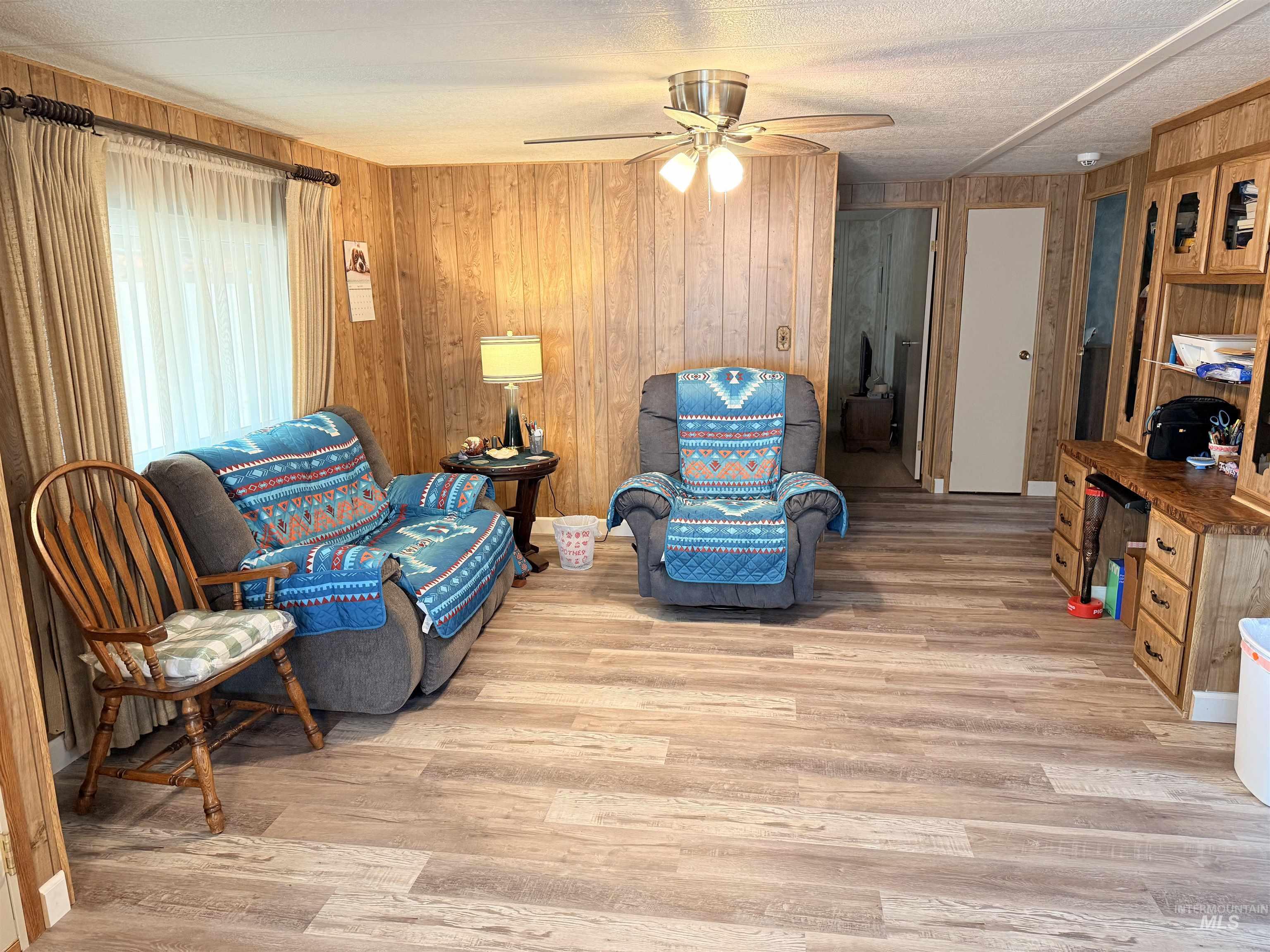 Living area featuring wooden walls, light wood finished floors, and ceiling fan