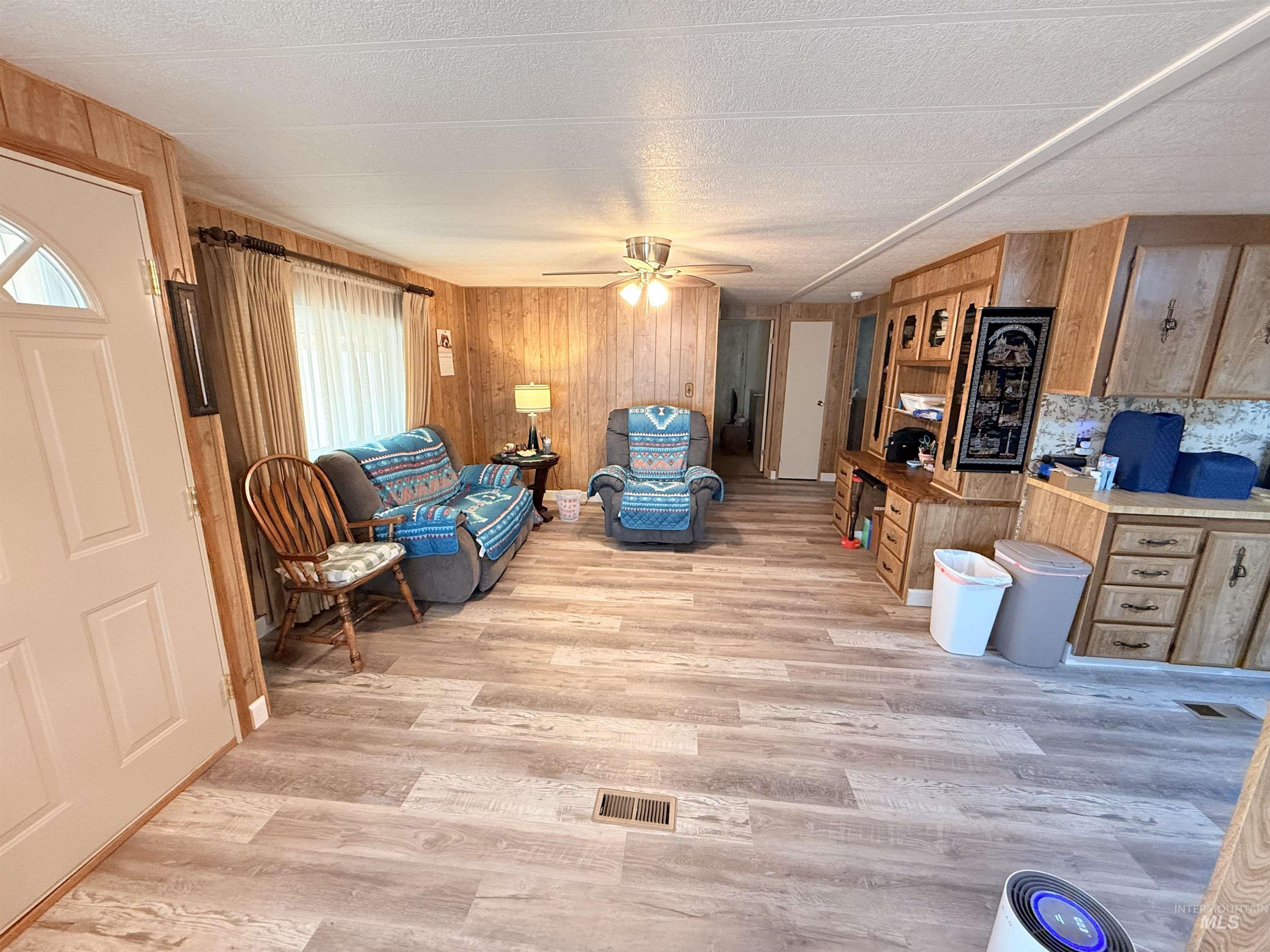 Living room featuring wood walls, light wood-style flooring, ceiling fan, and a textured ceiling