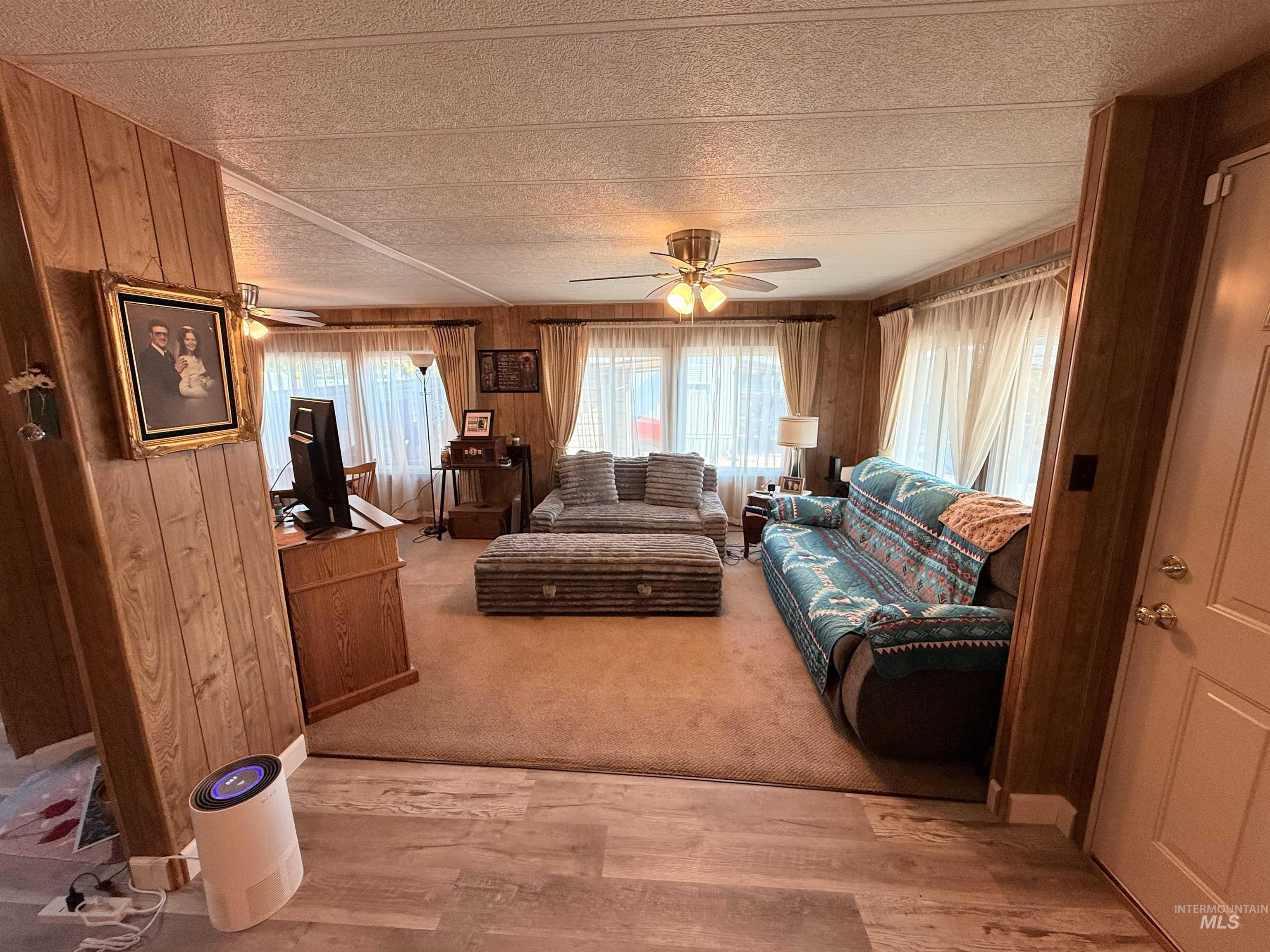 Living area featuring wooden walls, light wood-style flooring, a ceiling fan, and a textured ceiling