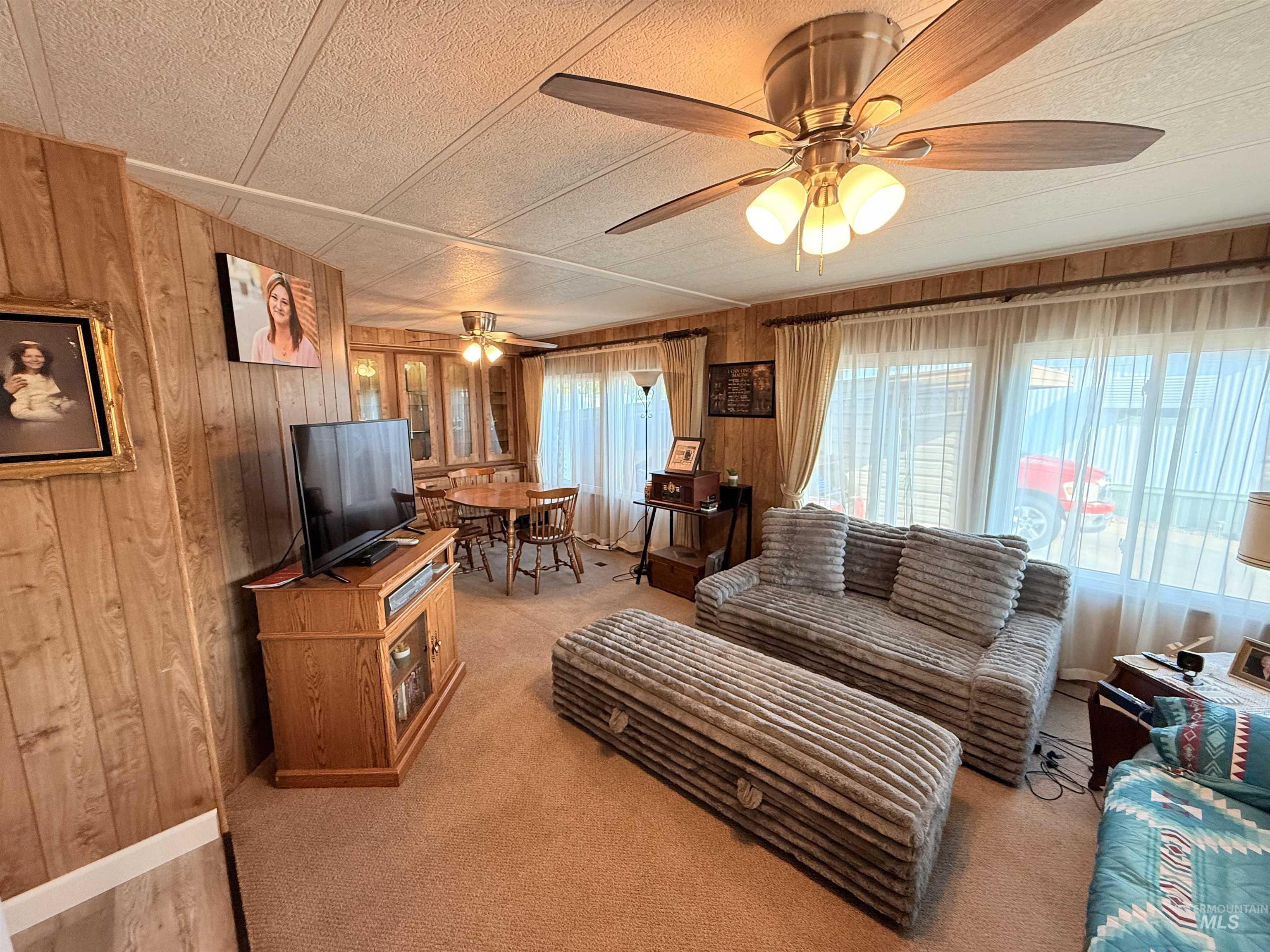 Living area featuring wooden walls, light carpet, and ceiling fan