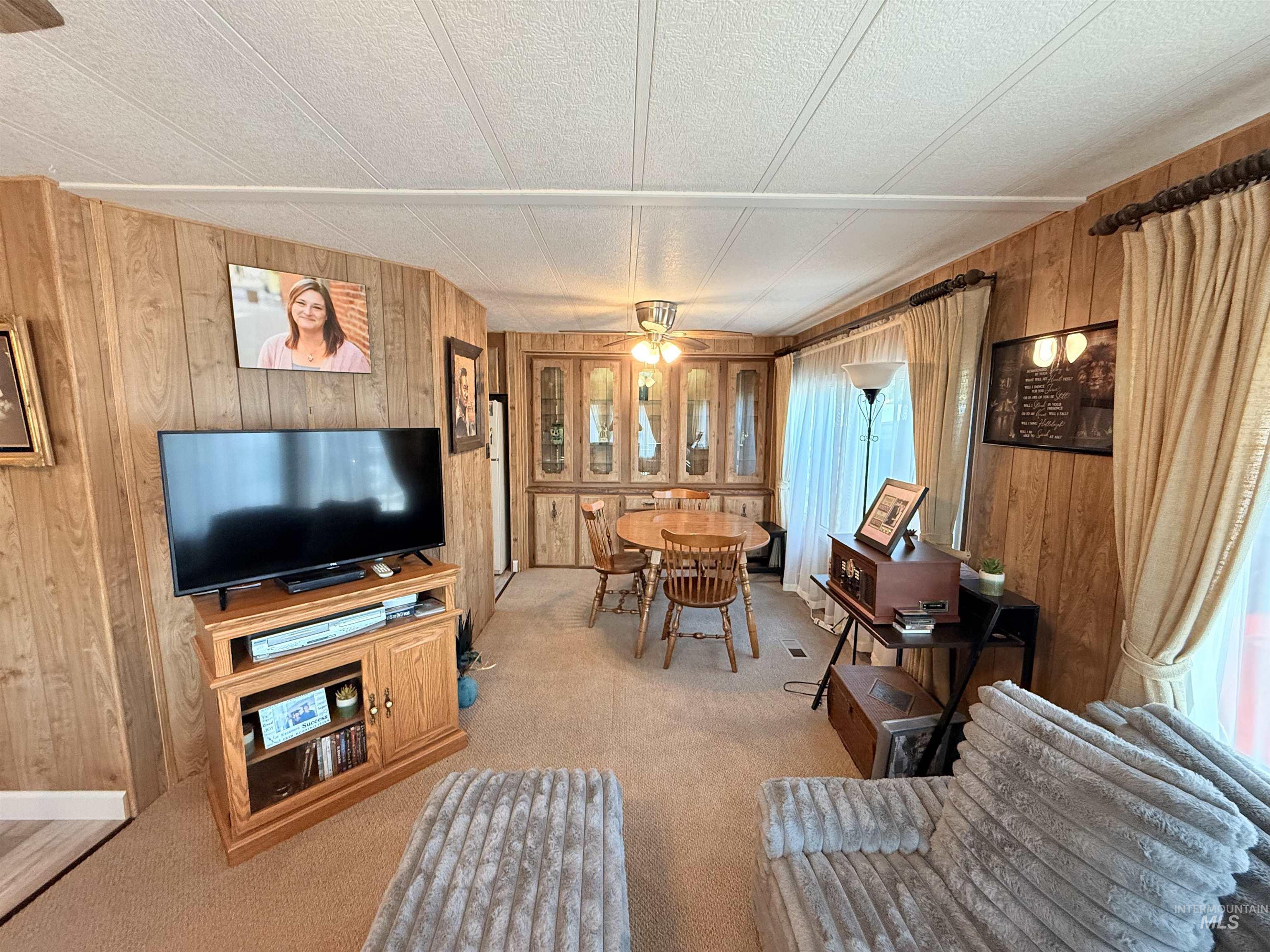 Living area with wooden walls, ceiling fan, and light colored carpet