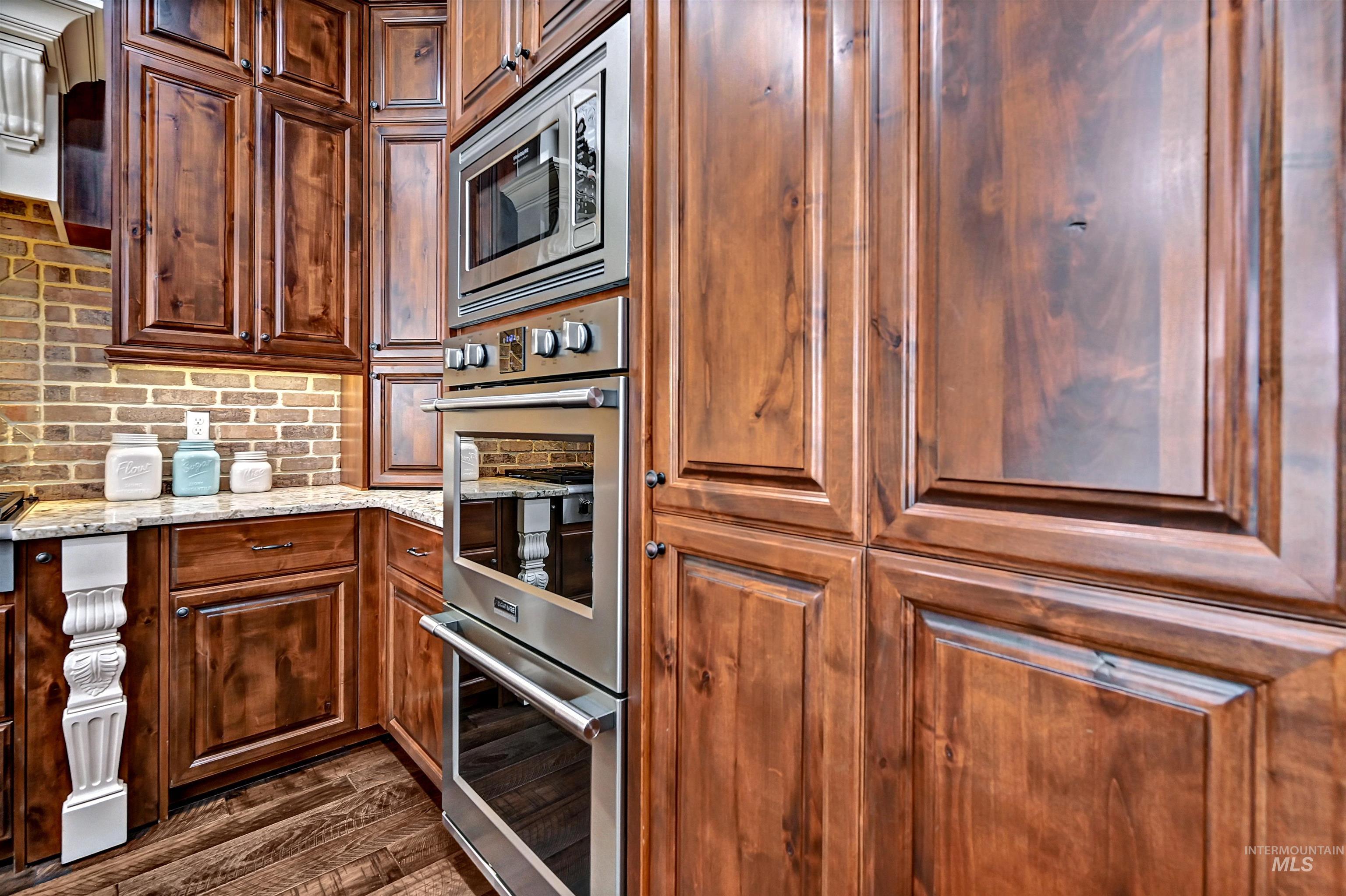 Kitchen featuring appliances with stainless steel finishes, light stone countertops, tasteful backsplash, exhaust hood, and dark wood finished floors