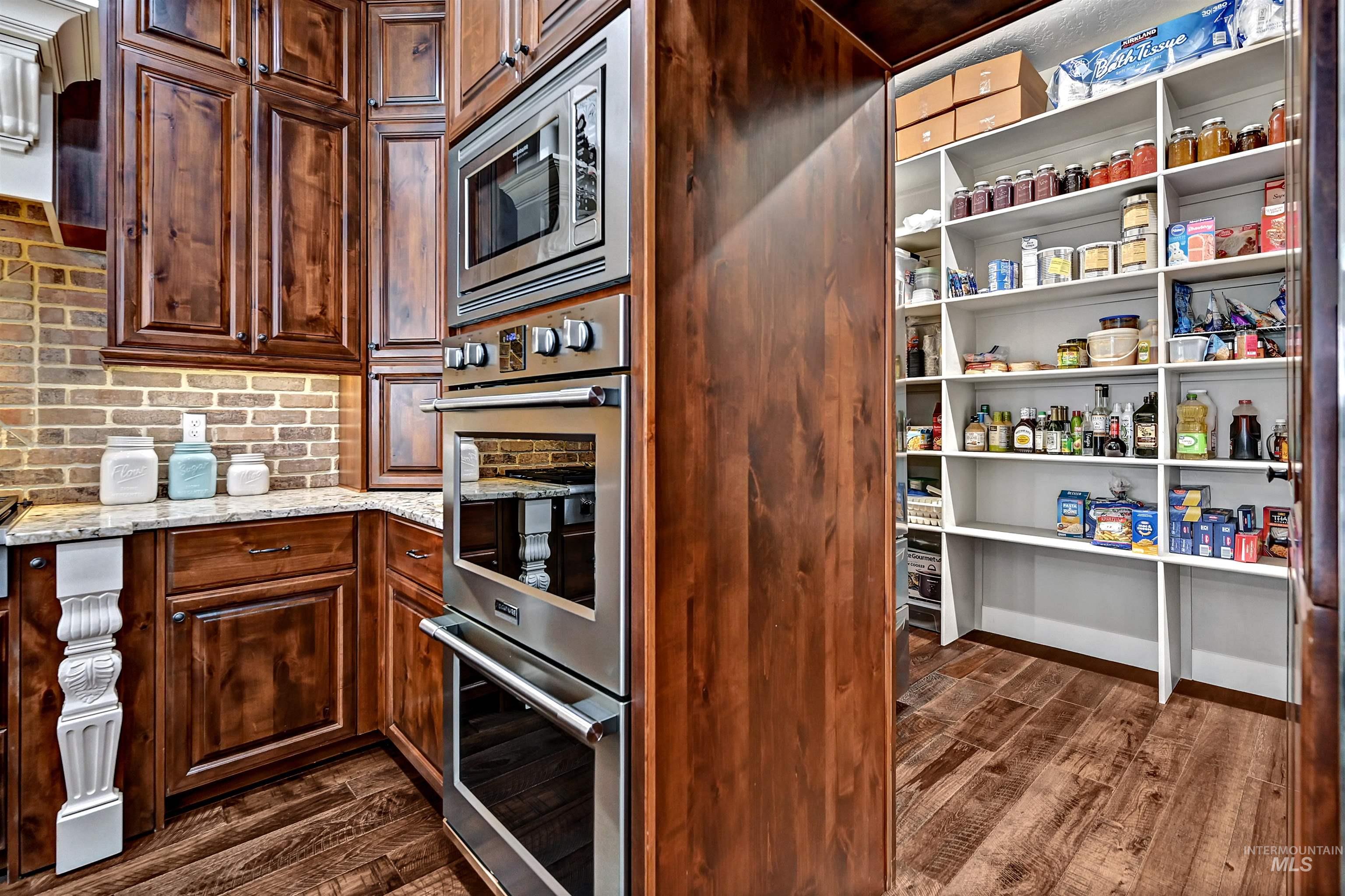 Kitchen featuring stainless steel appliances, dark wood-style floors, extractor fan, light stone countertops, and backsplash