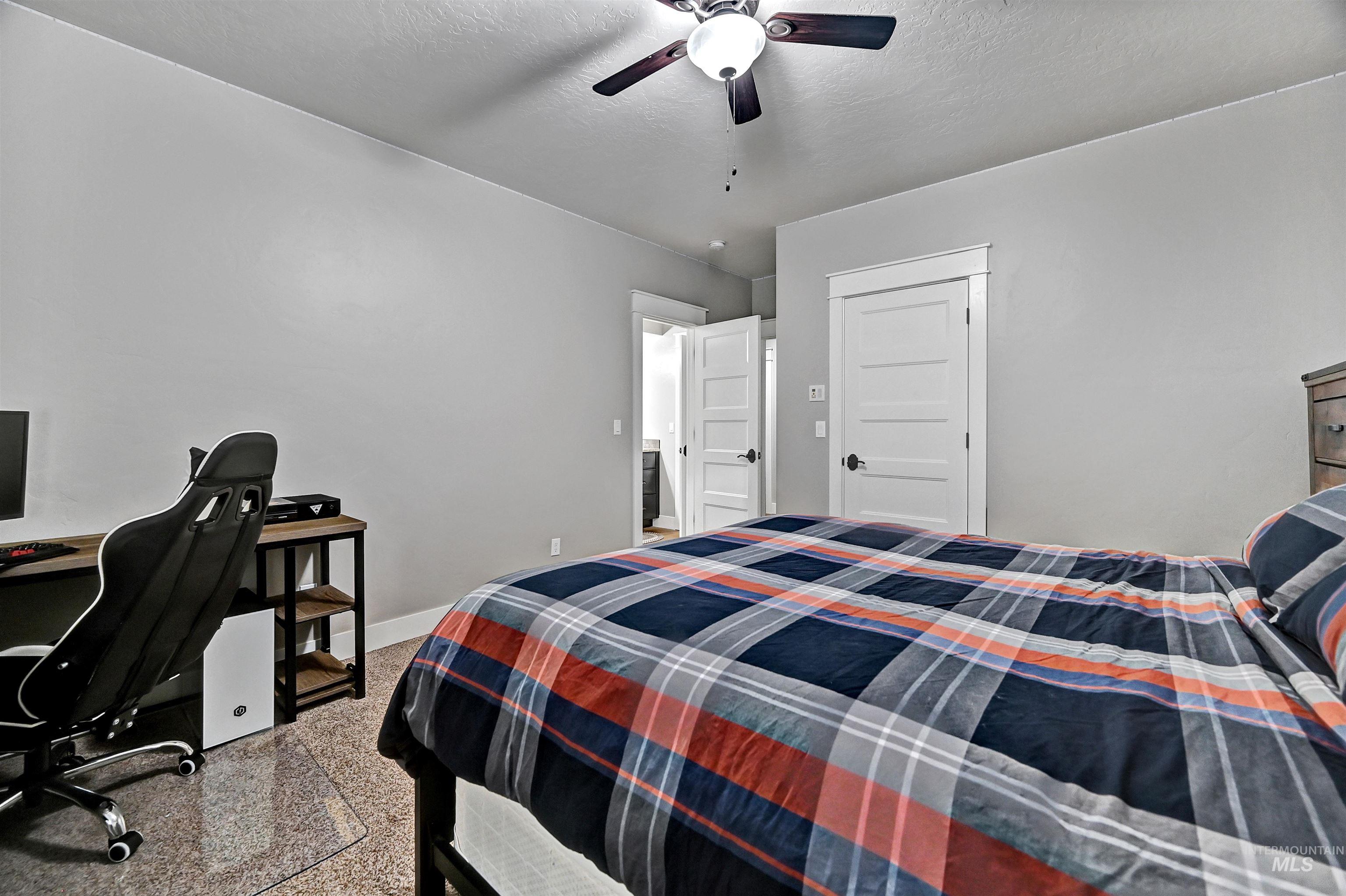 Bedroom with a desk, a ceiling fan, a textured ceiling, and dark speckled floor