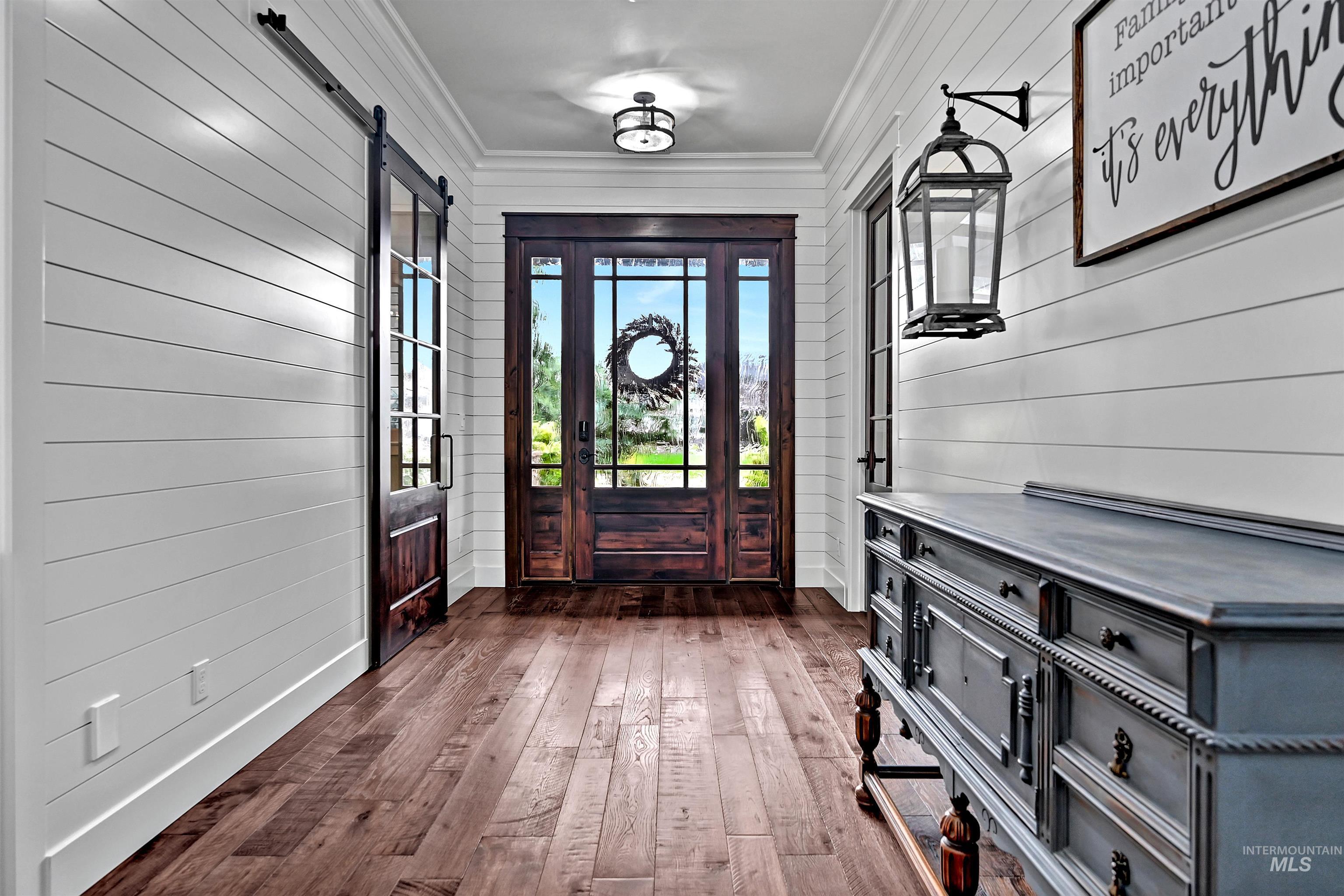 Entryway featuring dark wood-style floors, crown molding, wooden walls, and a barn door