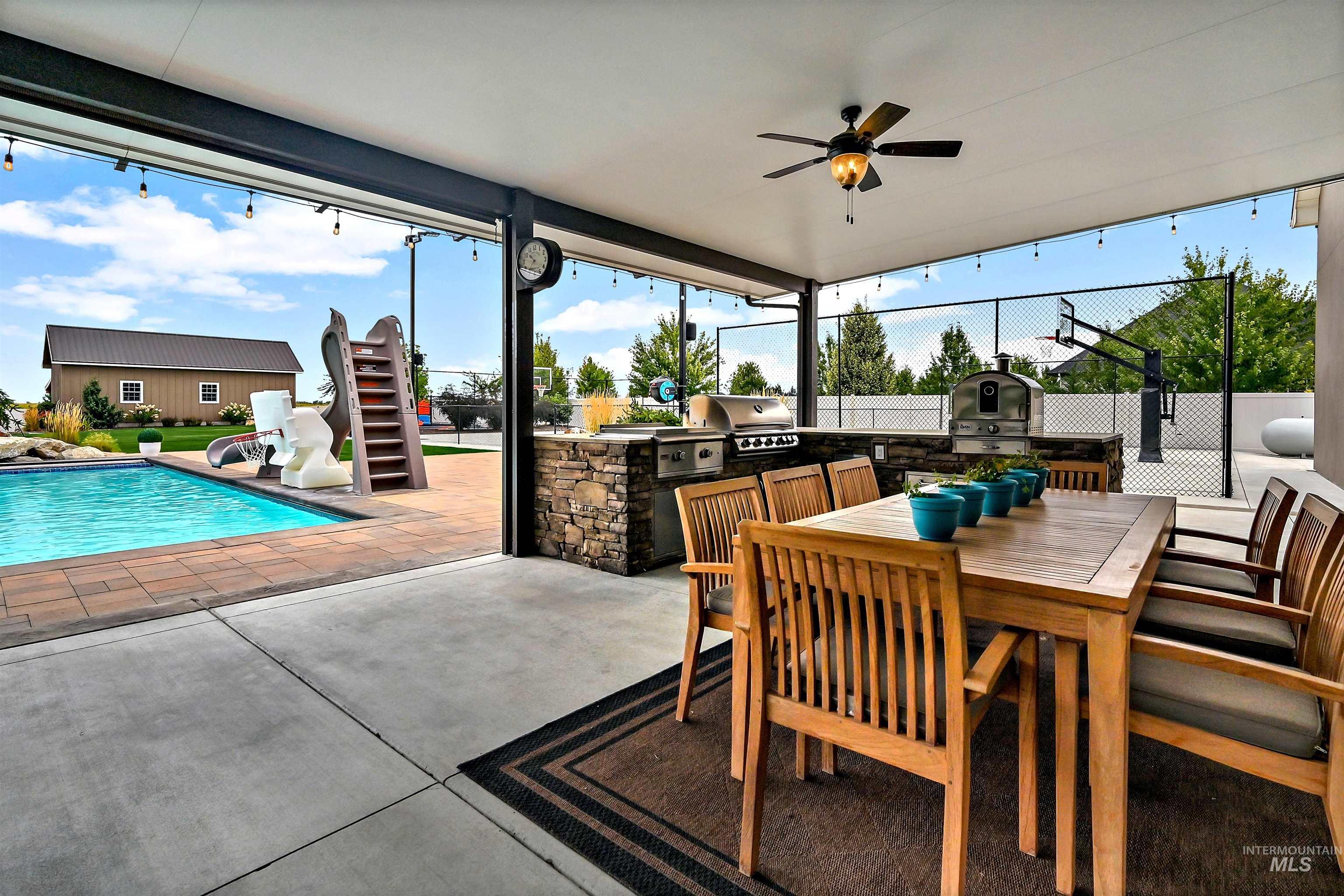 View of patio featuring exterior kitchen, outdoor dining area, a ceiling fan, an outdoor pool, and stairs