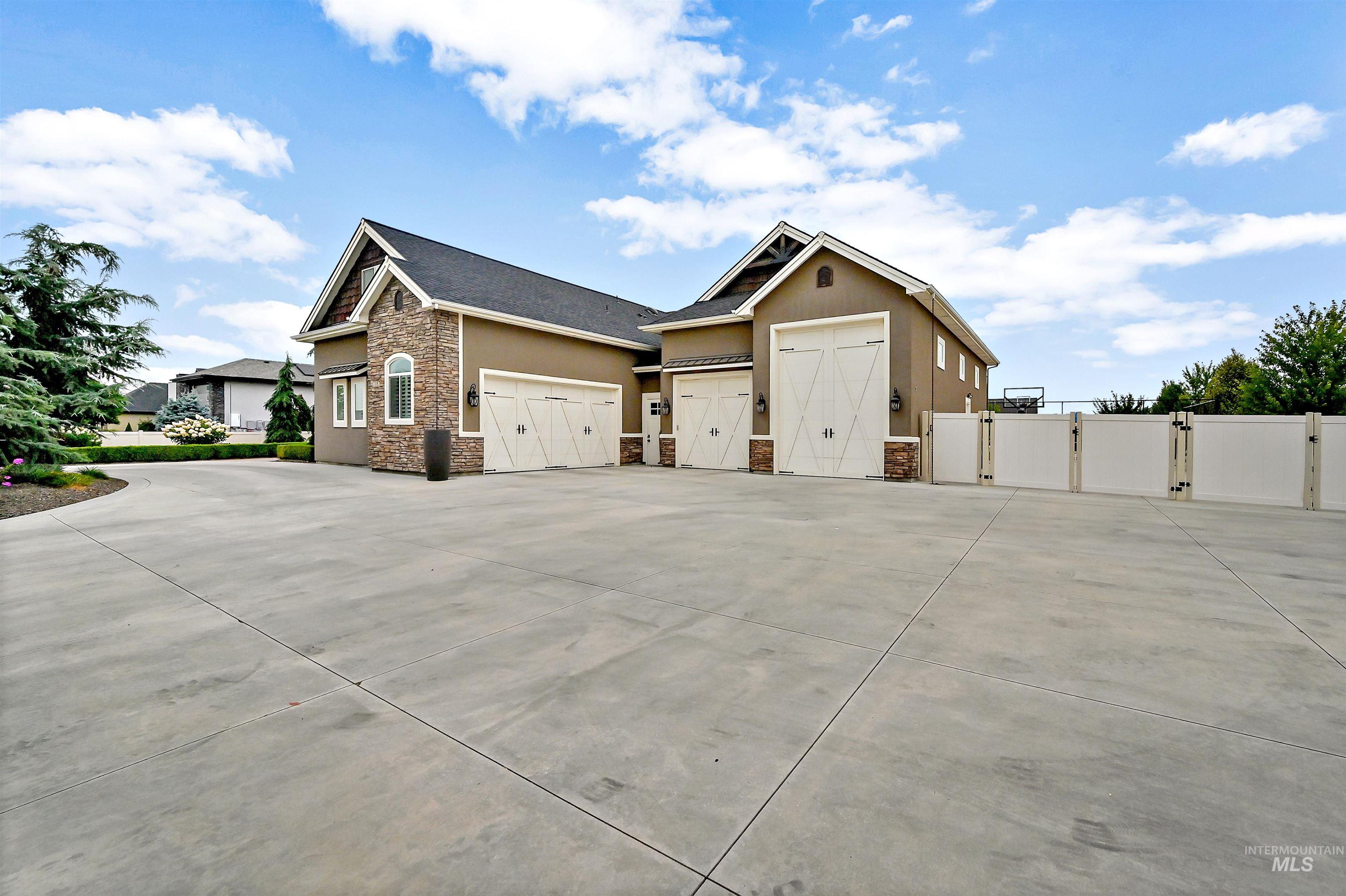 View of side of home with stone siding, a gate, driveway, stucco siding, and a garage