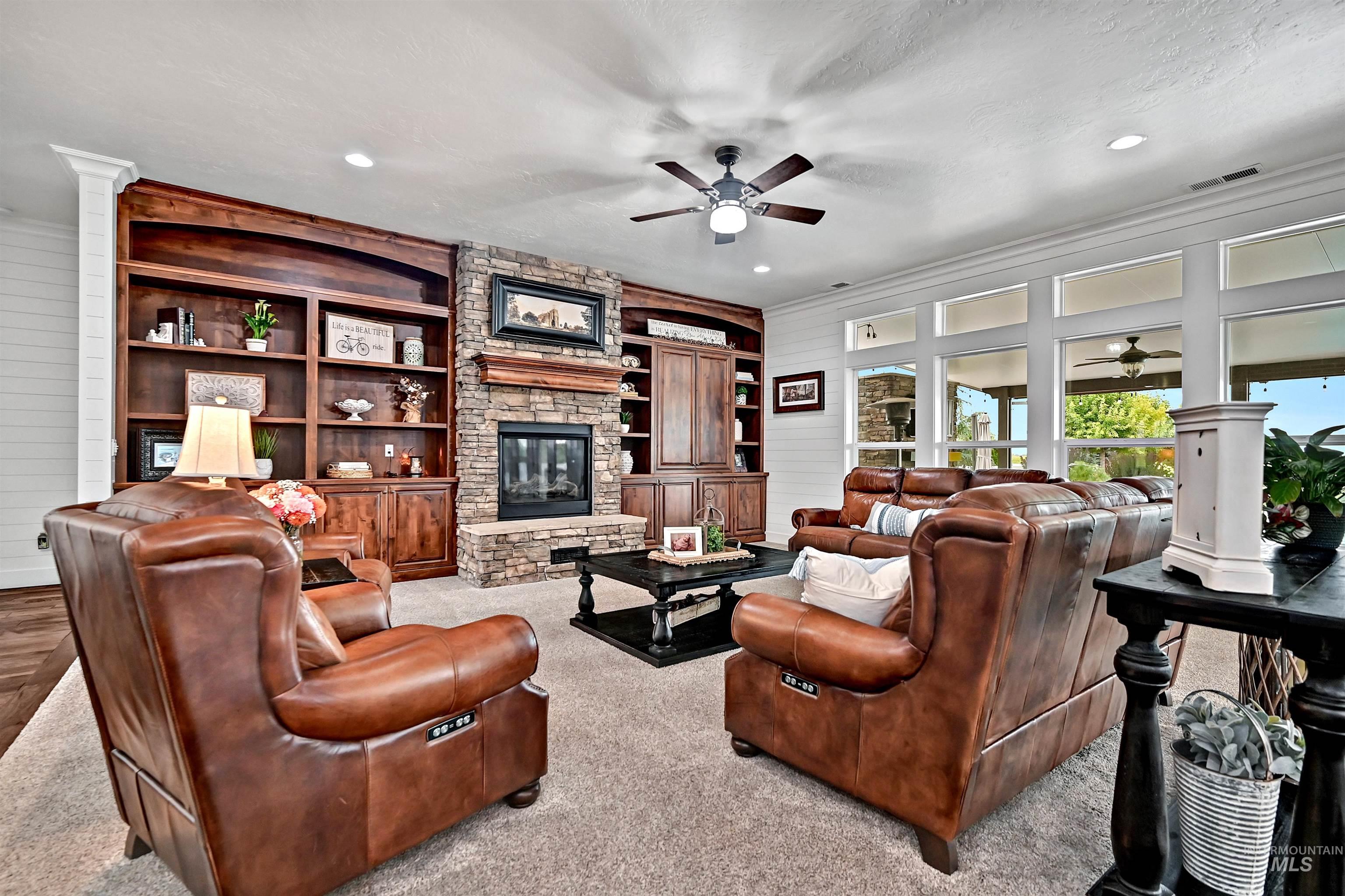 Living area featuring wooden walls, a stone fireplace, carpet flooring, a textured ceiling, and ceiling fan