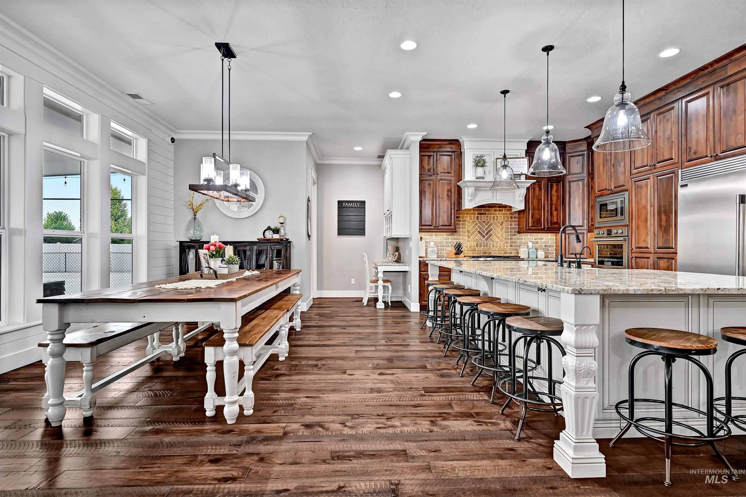 Kitchen with a breakfast bar, light stone counters, a spacious island, crown molding, and pendant lighting