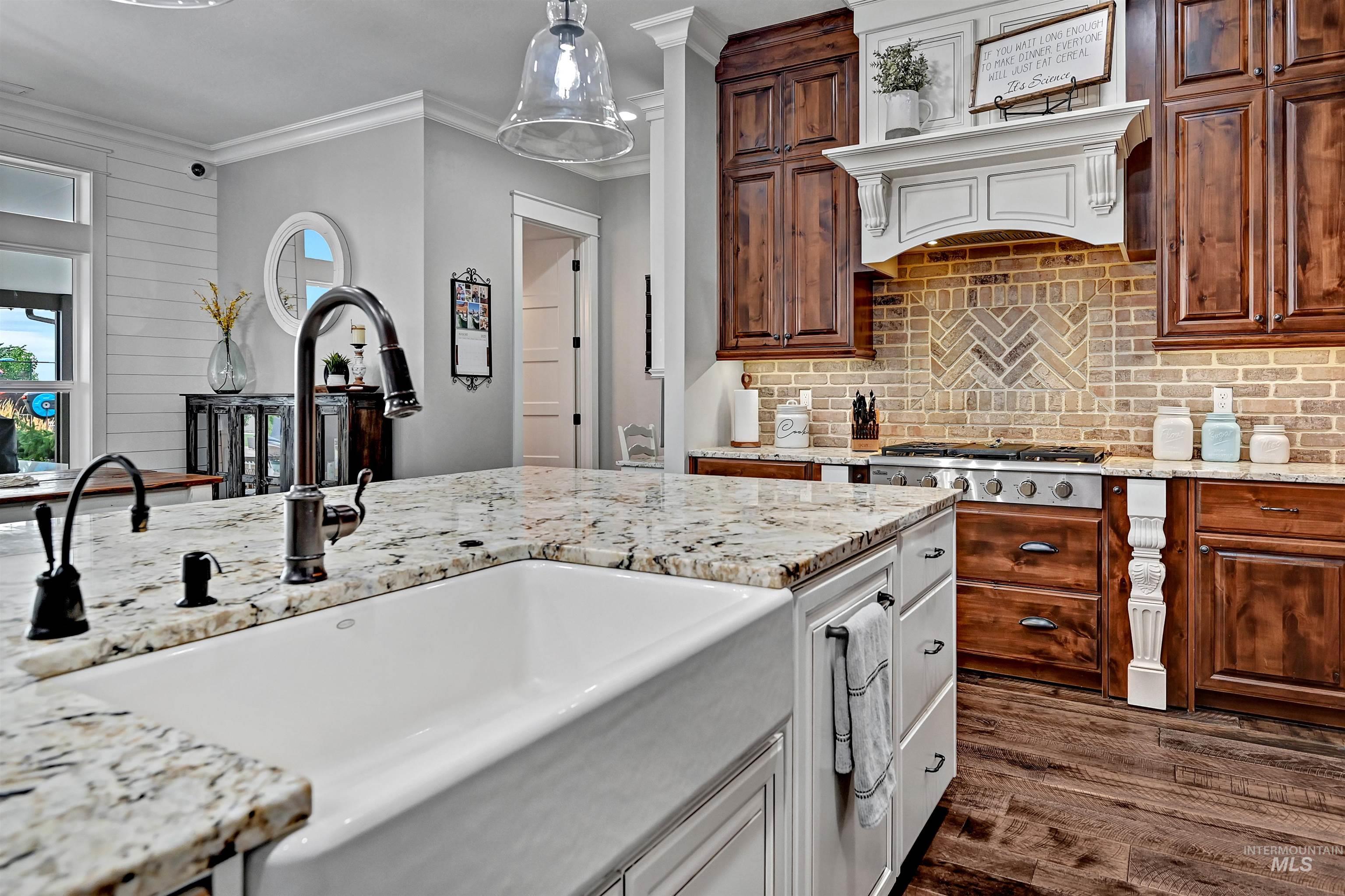 Kitchen featuring light stone countertops, crown molding, dark wood-type flooring, pendant lighting, and tasteful backsplash