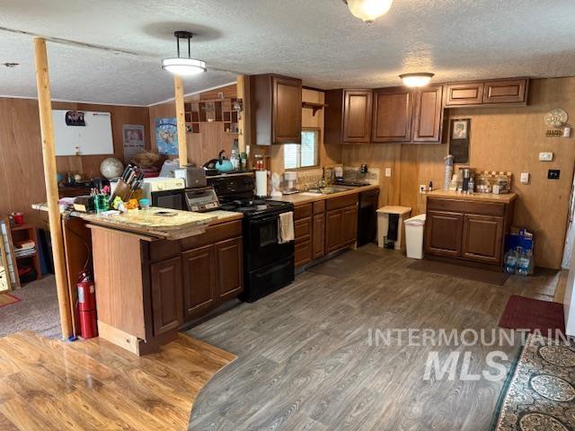 Kitchen featuring light countertops, wooden walls, black appliances, a peninsula, and dark wood-style floors