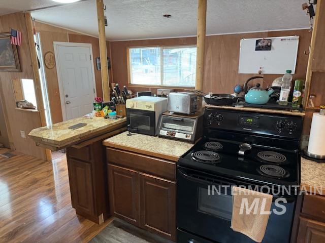 Kitchen with light countertops, black / electric stove, dark wood-style floors, a textured ceiling, and wooden walls