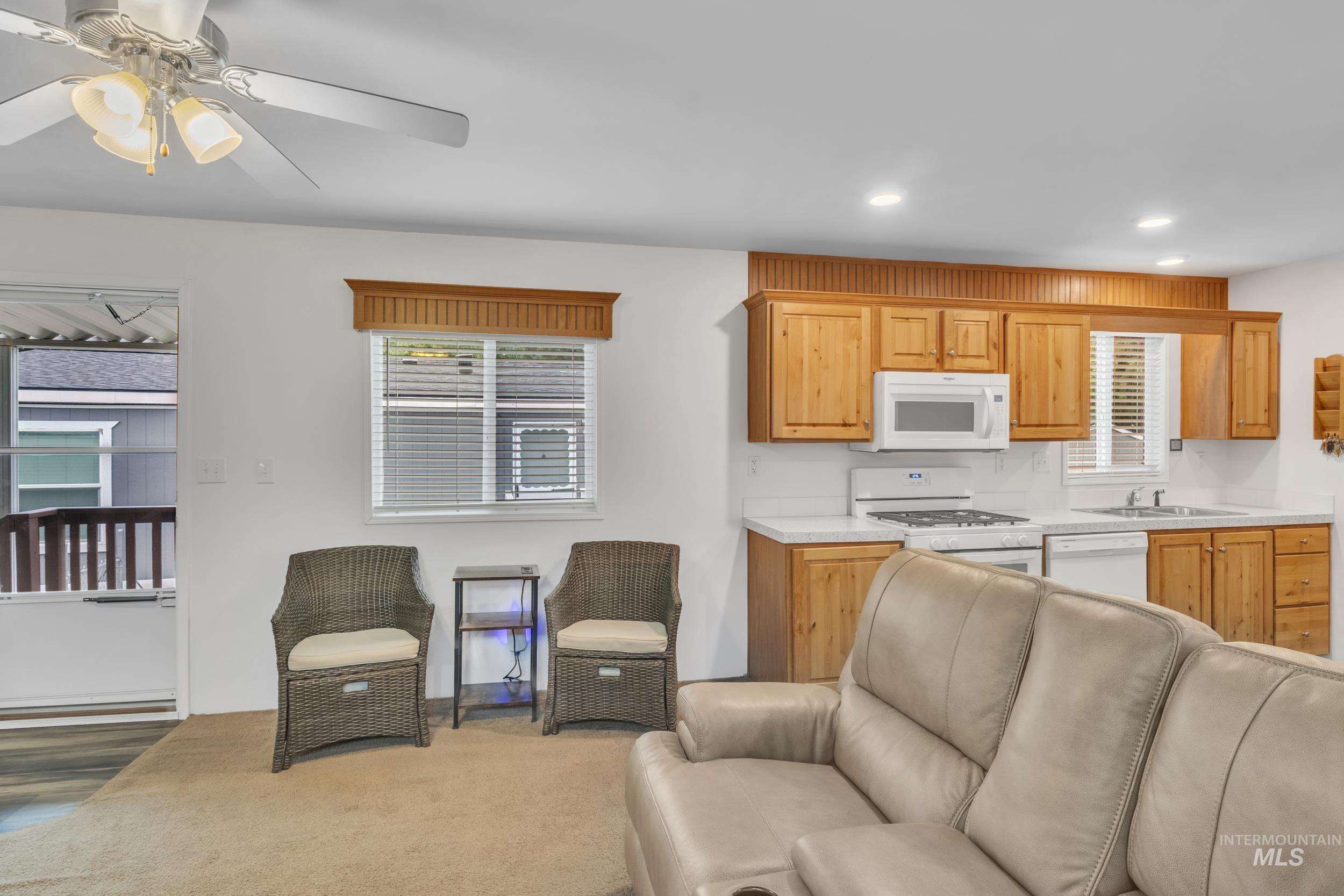 Kitchen with light countertops, open floor plan, white appliances, ceiling fan, and carpet floors