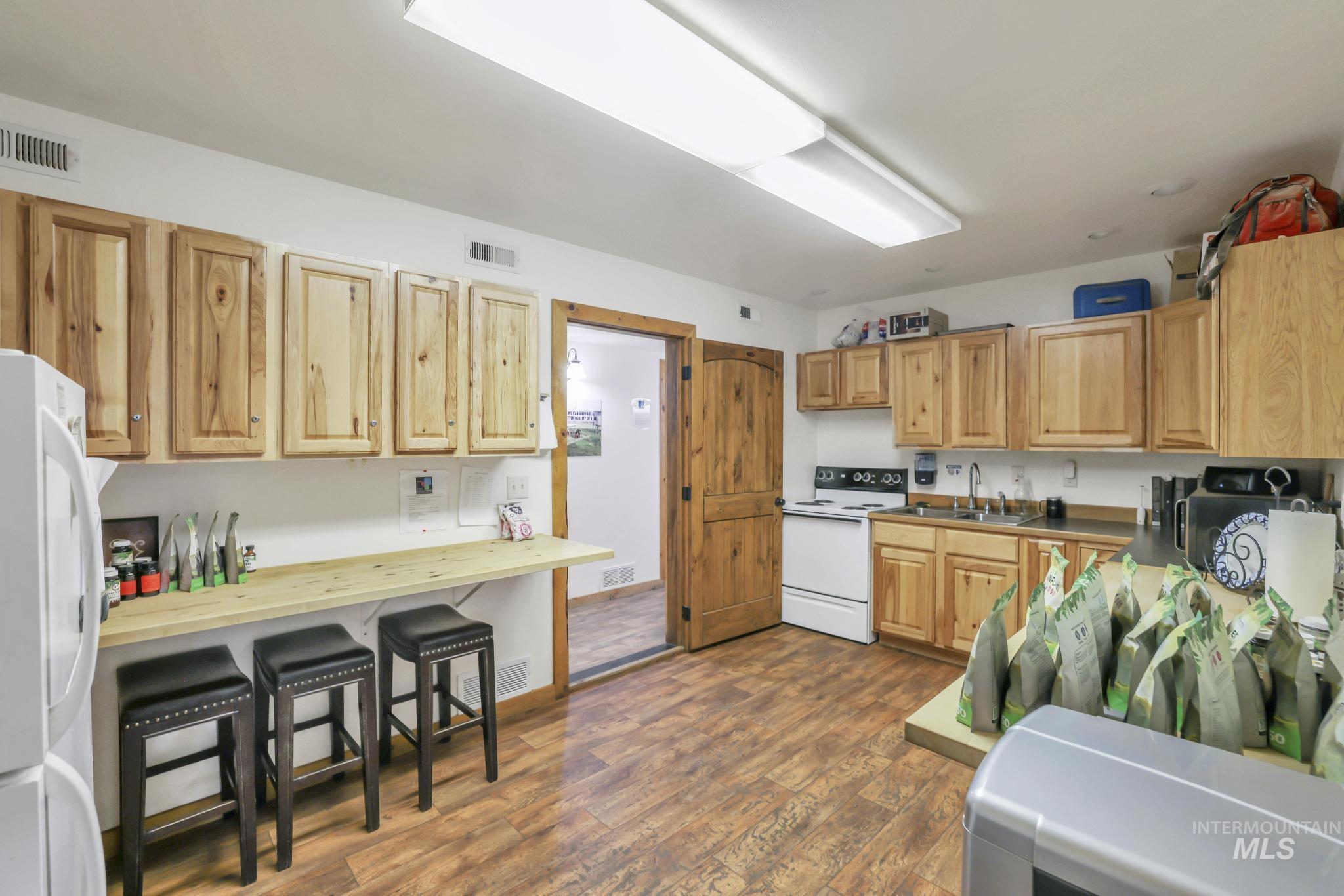 Kitchen featuring white appliances, dark wood-style floors, a kitchen bar, and light brown cabinetry