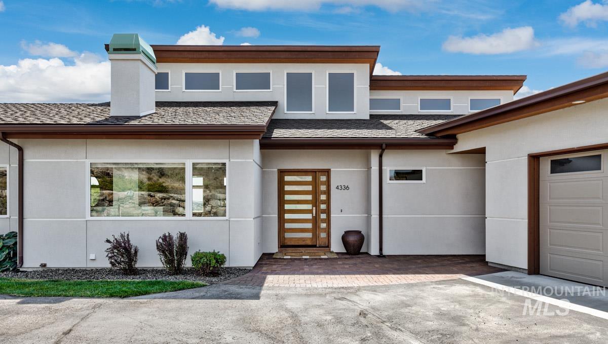 View of front of house featuring stucco siding, an attached garage, roof with shingles, a chimney, and driveway