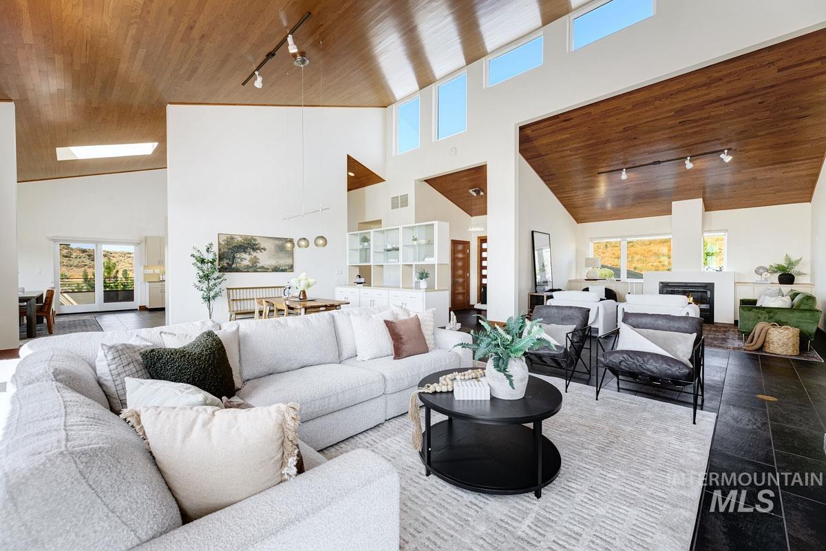 Living room with track lighting, wooden ceiling, high vaulted ceiling, plenty of natural light, and a glass covered fireplace