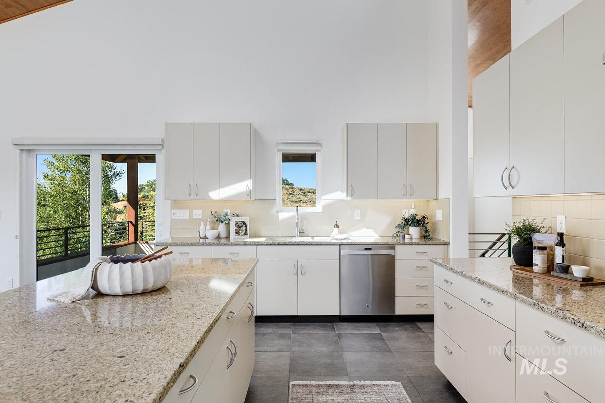 Kitchen with backsplash, dishwasher, light stone countertops, a high ceiling, and white cabinetry