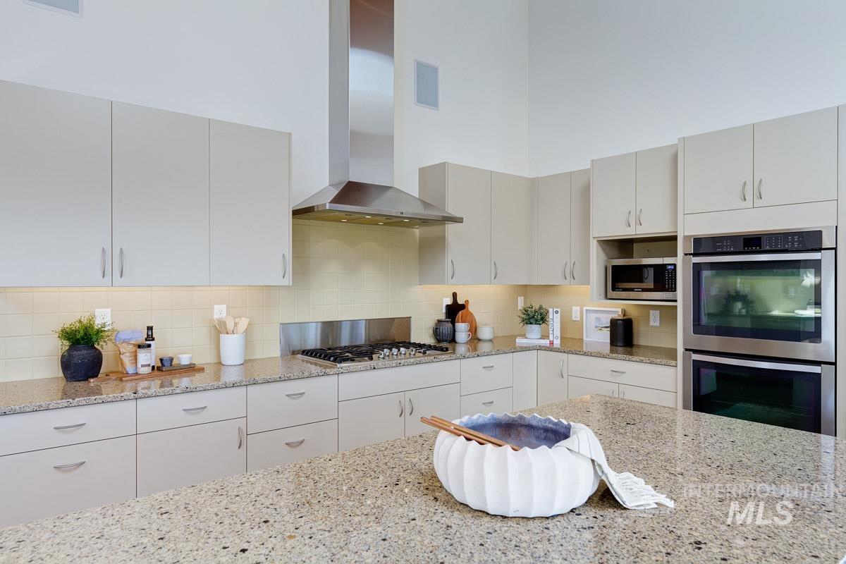 Kitchen featuring wall chimney range hood, tasteful backsplash, stainless steel appliances, light stone counters, and white cabinets