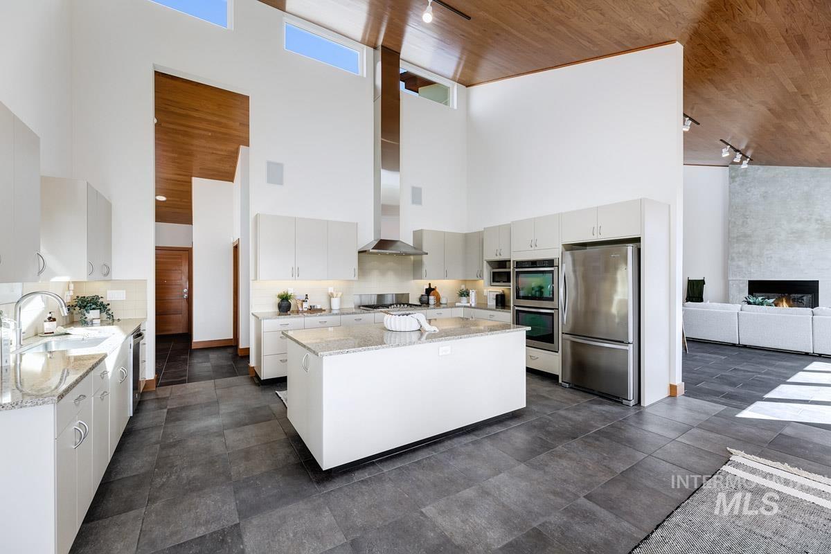 Kitchen featuring track lighting, stainless steel appliances, light stone countertops, a kitchen island, and a towering ceiling