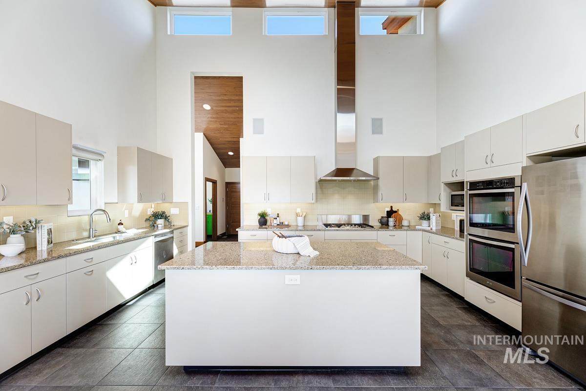 Kitchen featuring tasteful backsplash, stainless steel appliances, light stone countertops, a center island, and a high ceiling