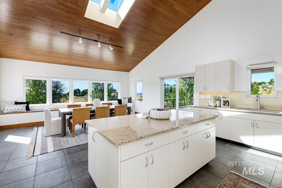 Kitchen featuring a skylight, high vaulted ceiling, wood ceiling, white cabinets, and light stone counters