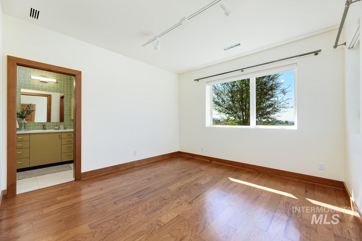 Unfurnished bedroom with track lighting, light wood finished floors, and ensuite bath