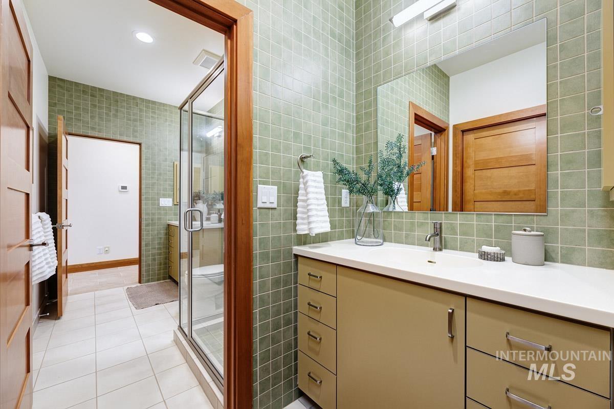 Bathroom with tile walls, light tile patterned floors, vanity, a shower stall, and recessed lighting