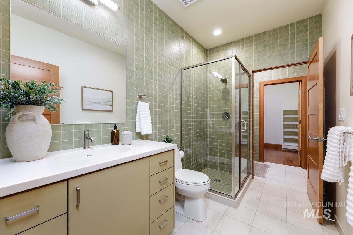 Bathroom featuring vanity, tile walls, light tile patterned floors, a shower stall, and decorative backsplash