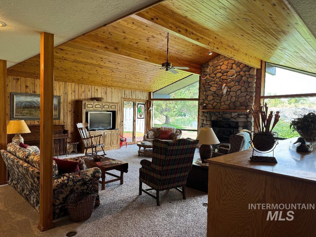 Living area with a fireplace, carpet flooring, wood walls, and wooden ceiling