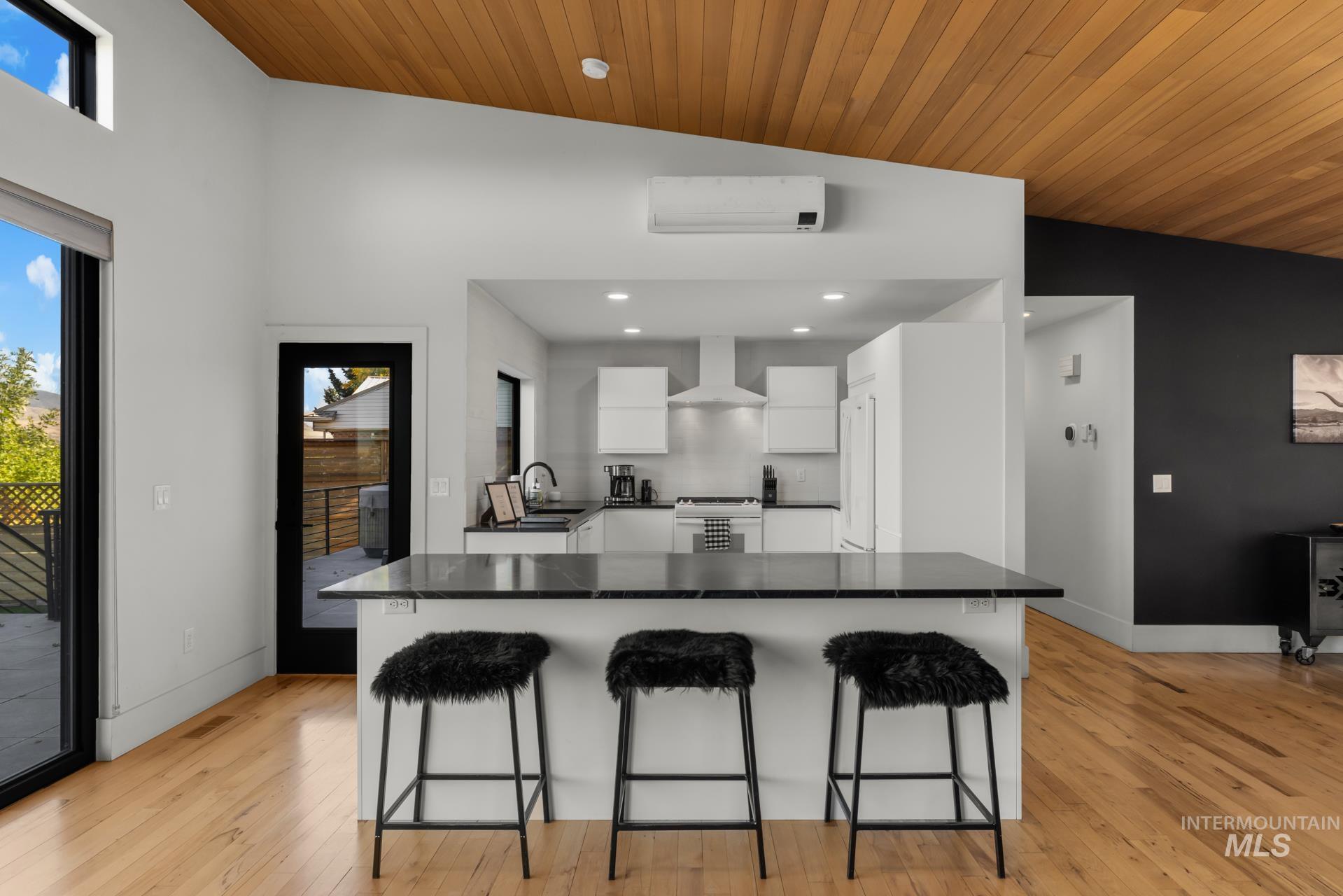 Kitchen with white cabinets, a breakfast bar area, light wood-type flooring, wood ceiling, and wall chimney range hood