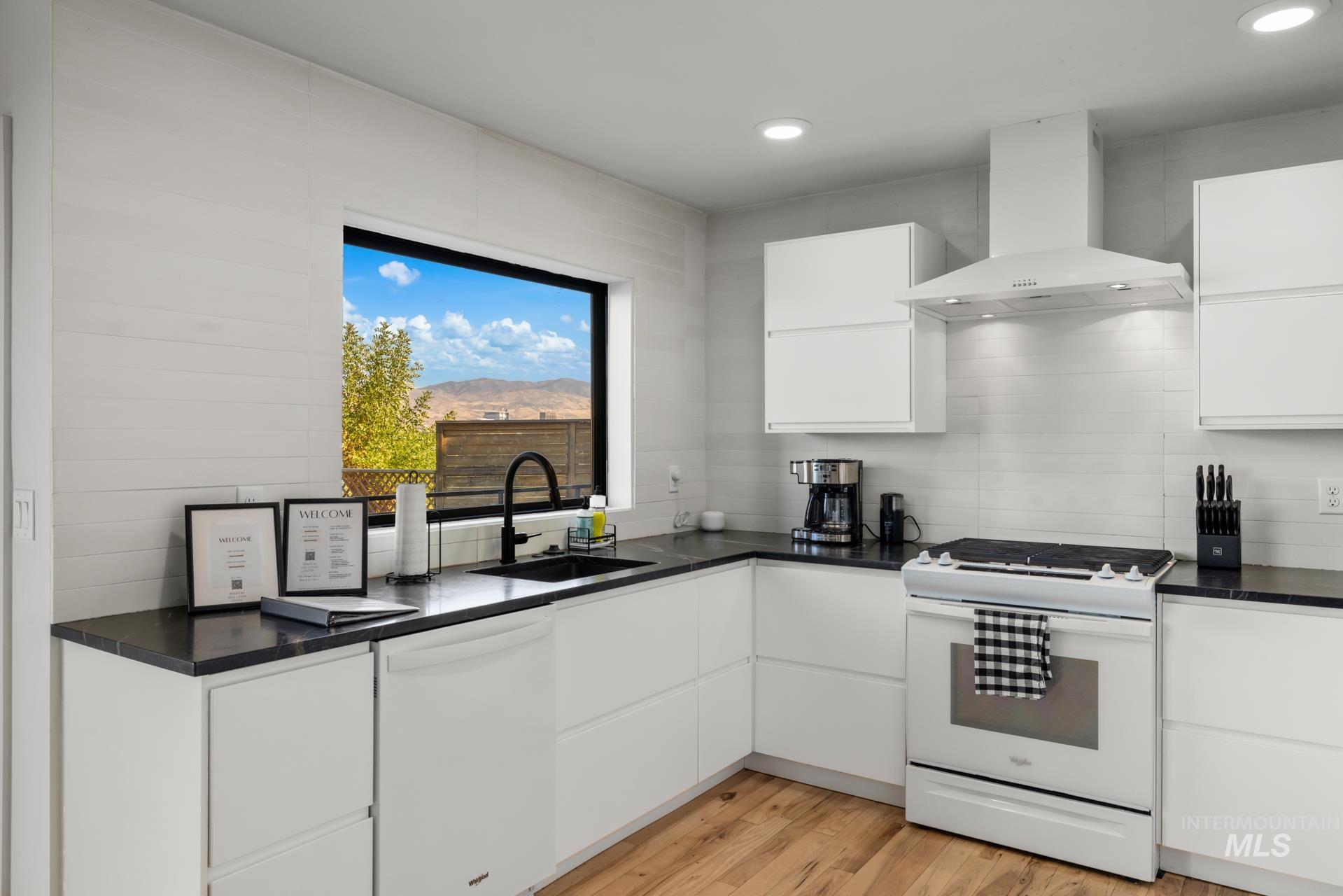 Kitchen with white cabinetry, white appliances, wall chimney range hood, light wood-style floors, and recessed lighting