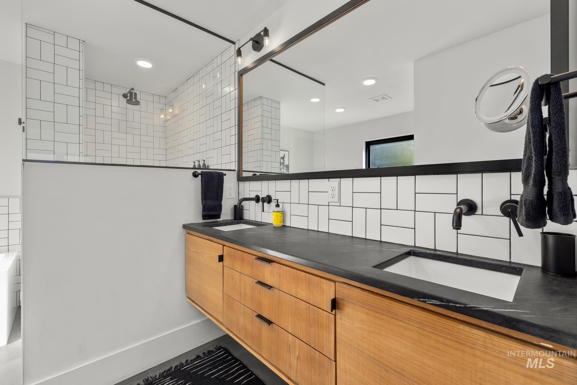 Bathroom with double vanity, decorative backsplash, a tile shower, tile walls, and recessed lighting