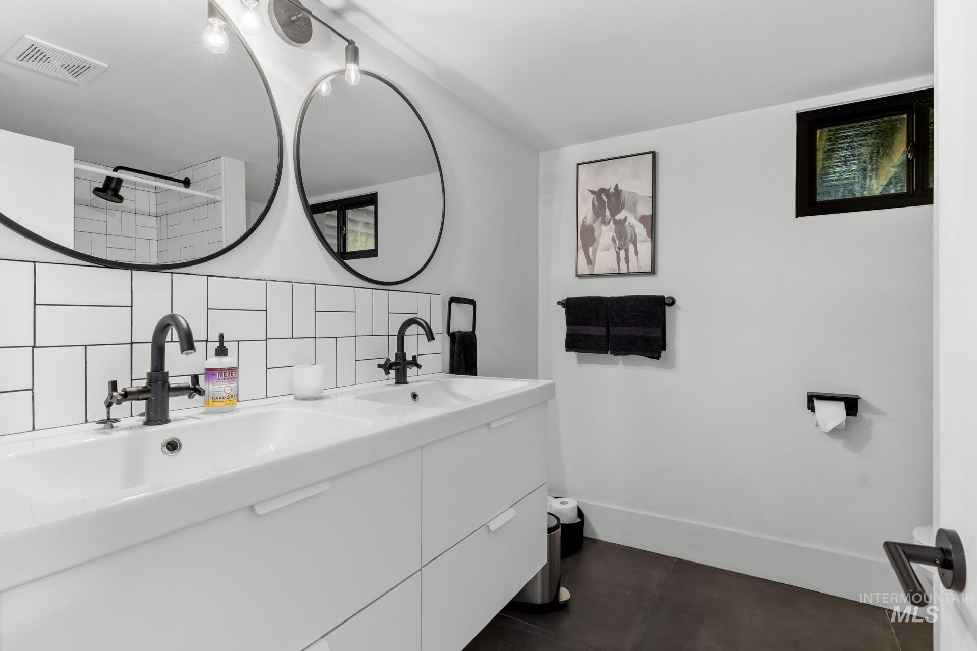 Full bath with decorative backsplash, double vanity, dark tile patterned flooring, and a shower