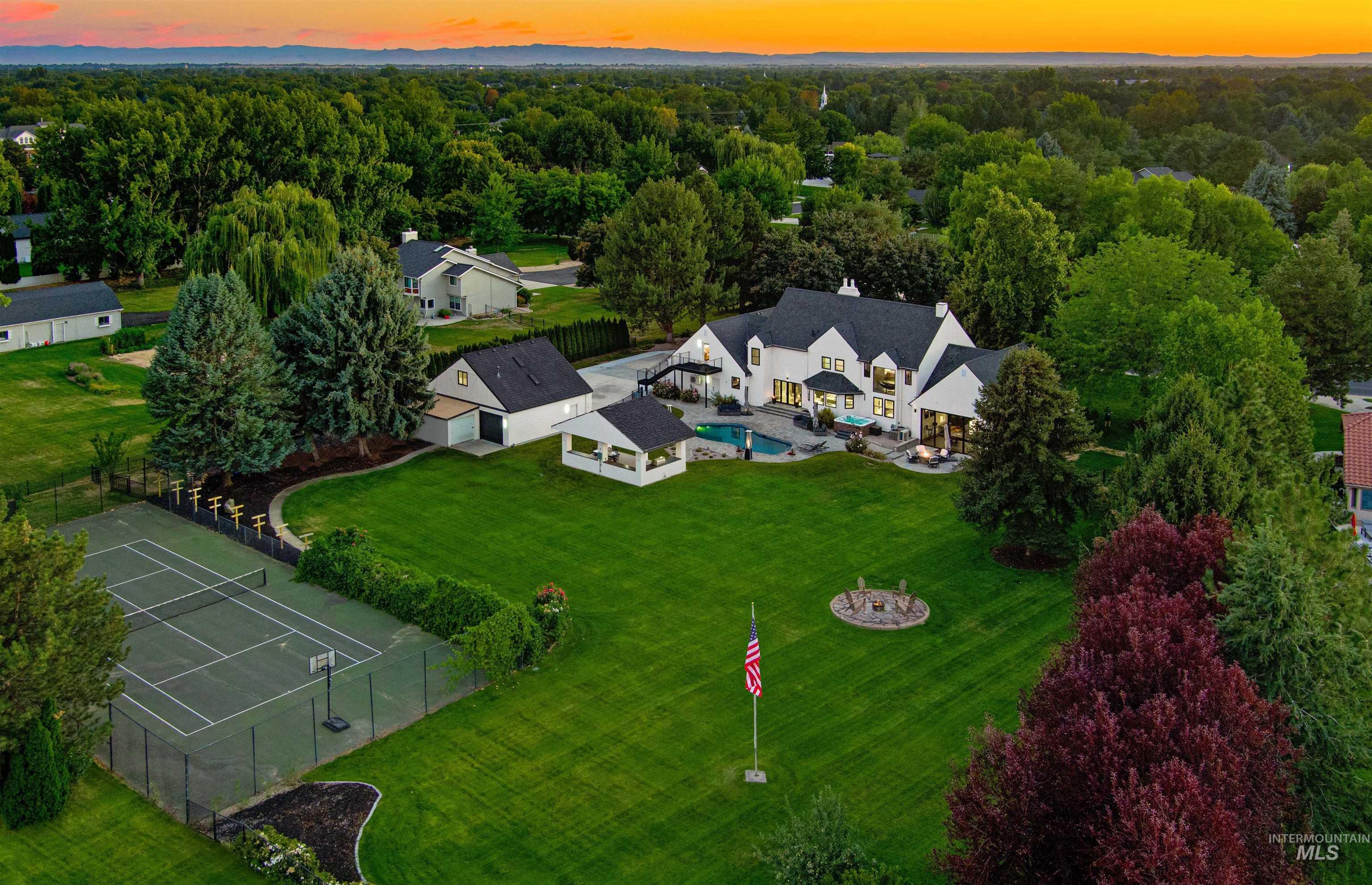 Aerial view at dusk featuring main home, detached garage, cabana, pool, hot tub, patio, full-size tennis court, garden areas, fire pit, private ADU entrance, and sprawling green yard with privacy.