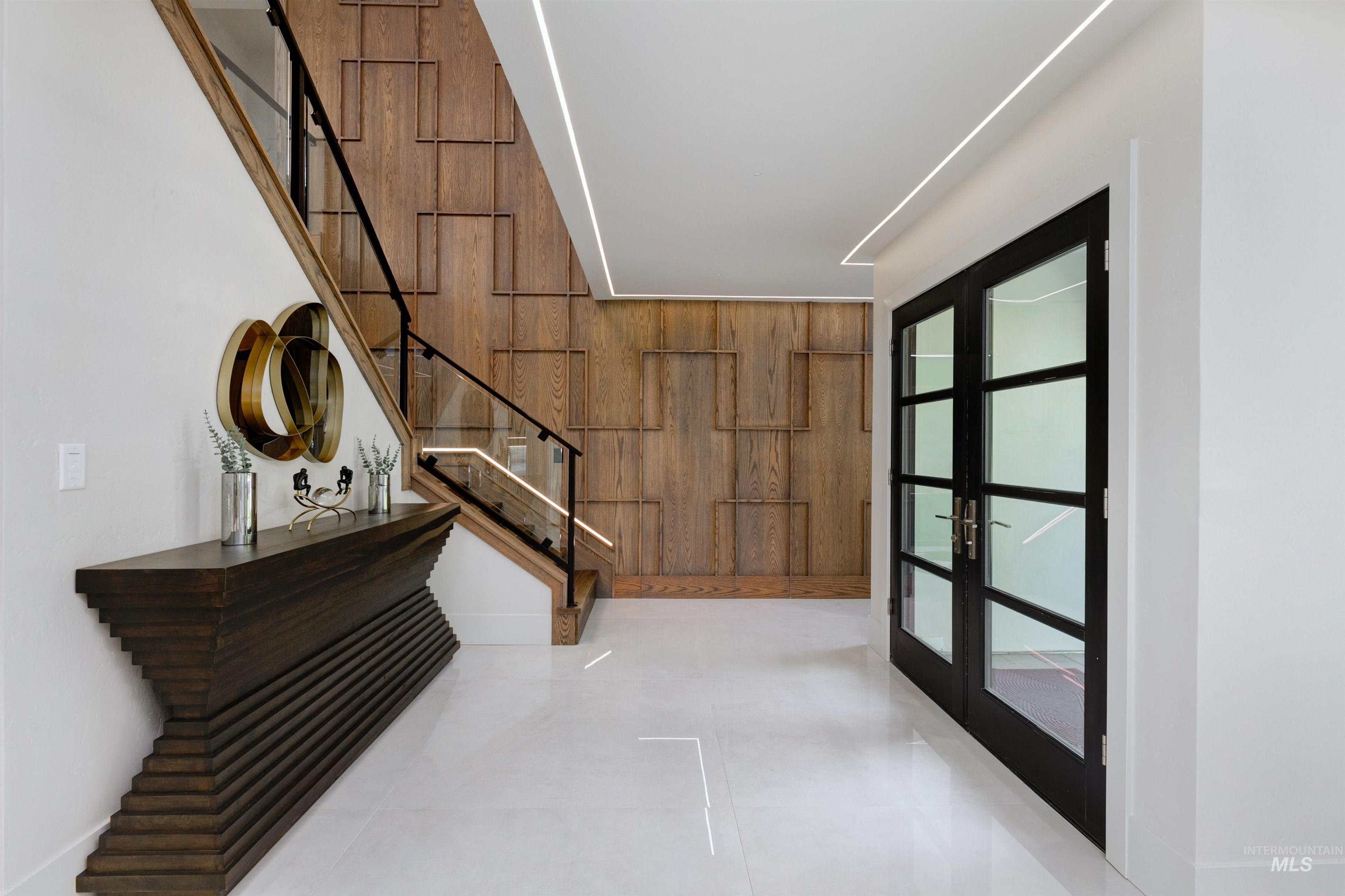 Entrance foyer featuring wood walls, stairway, light tile patterned flooring, and french doors.