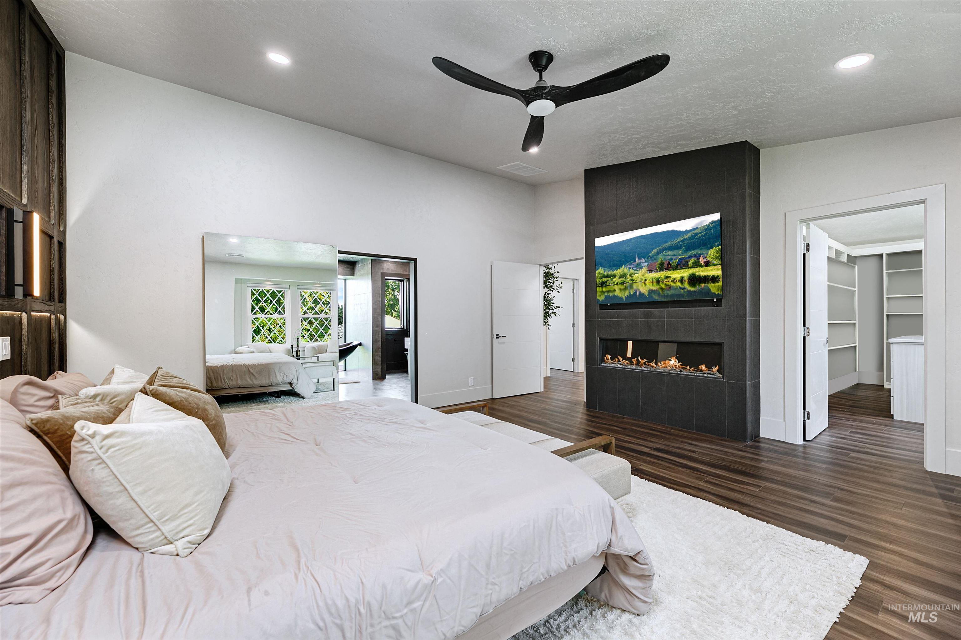 Master bedroom with dark wood finished floors, a spacious walk-in closet, a fireplace, and recessed lighting.