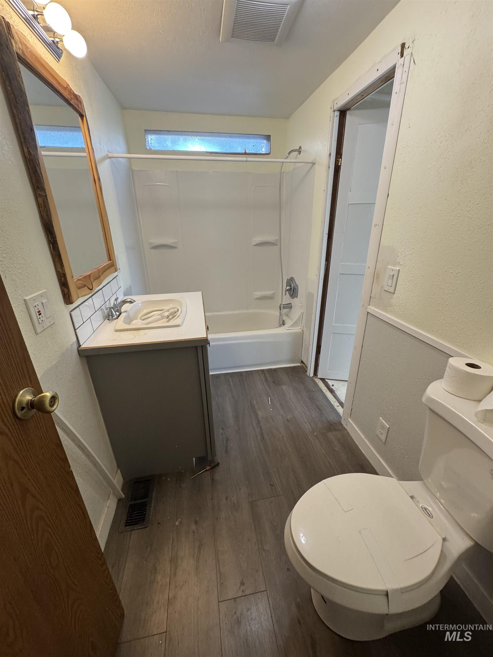 Full bath with a textured wall, shower / bathtub combination, dark wood-style floors, and vanity