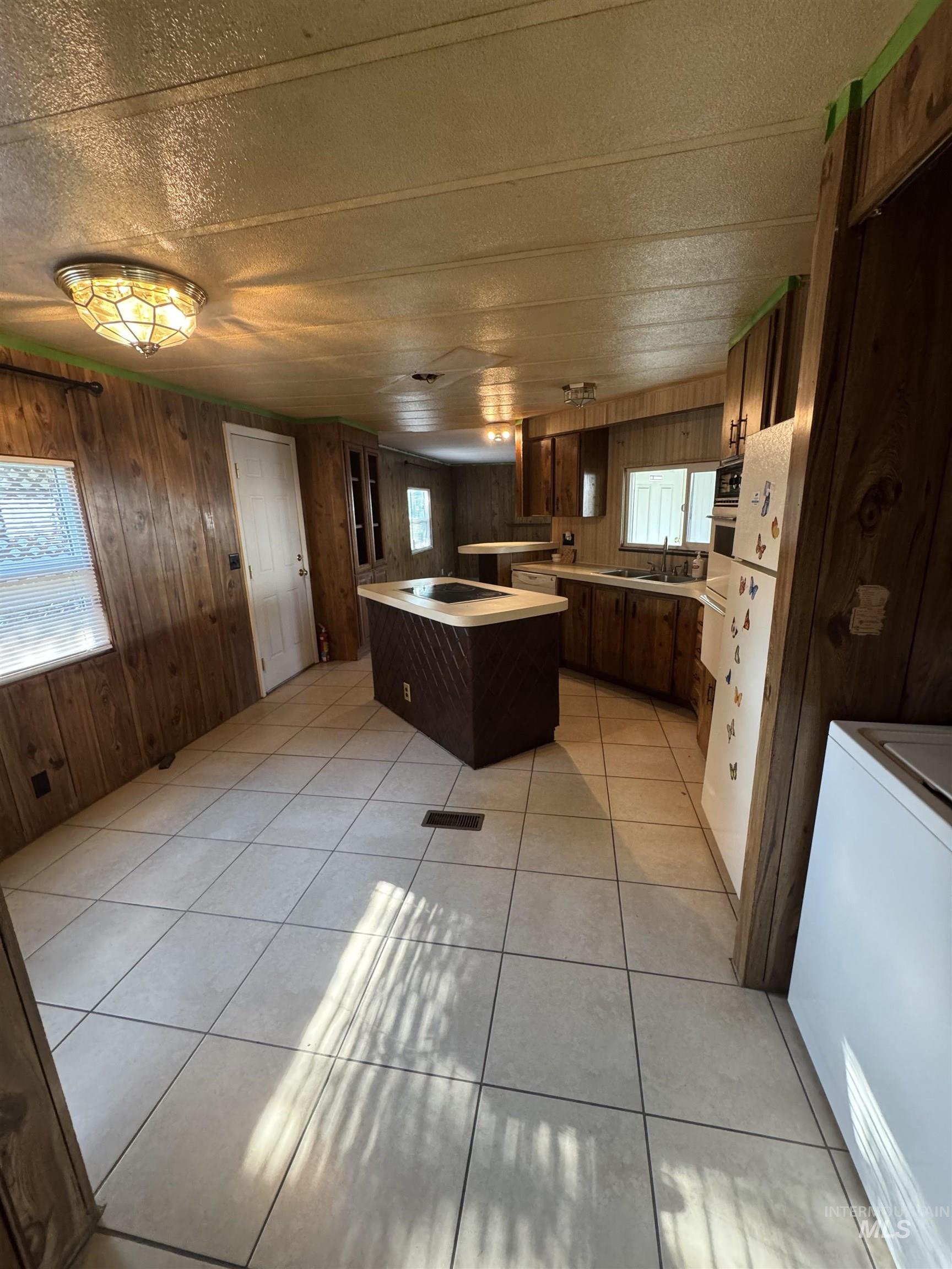 Kitchen featuring light countertops, light tile patterned floors, healthy amount of natural light, wooden walls, and a textured ceiling