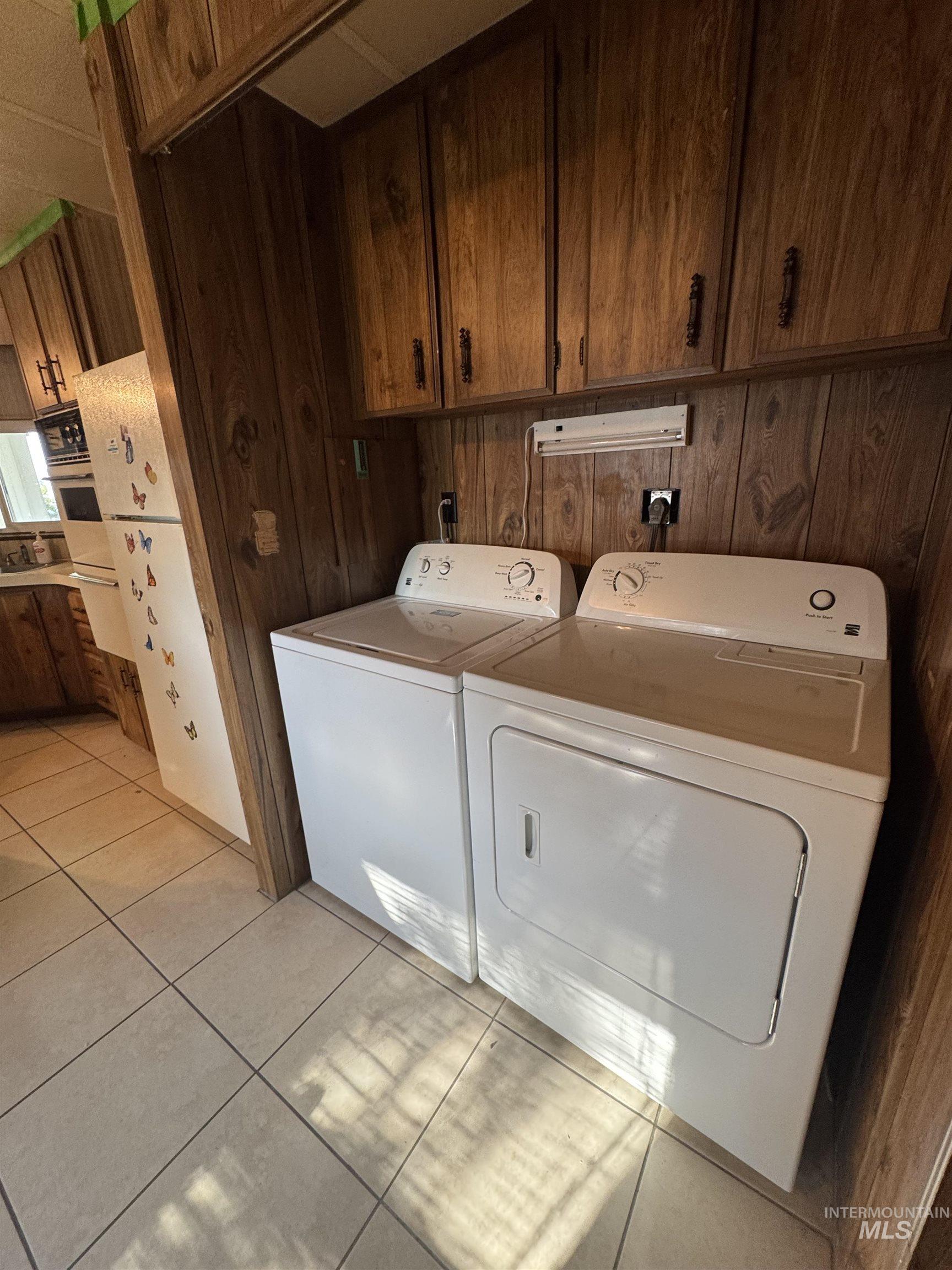 Washroom featuring wood walls, light tile patterned floors, washing machine and dryer, and cabinet space