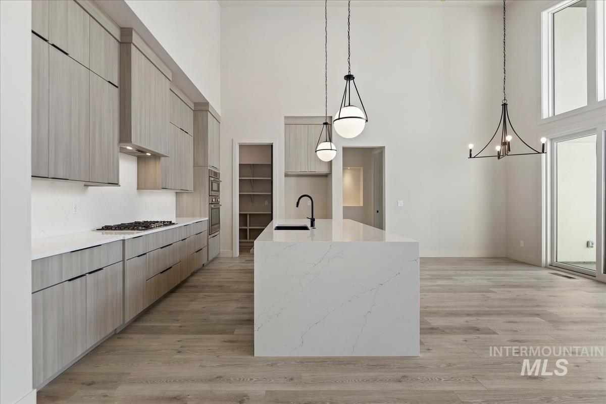 Kitchen with a towering ceiling, hanging light fixtures, a center island with sink, modern cabinets, and light wood-style floors