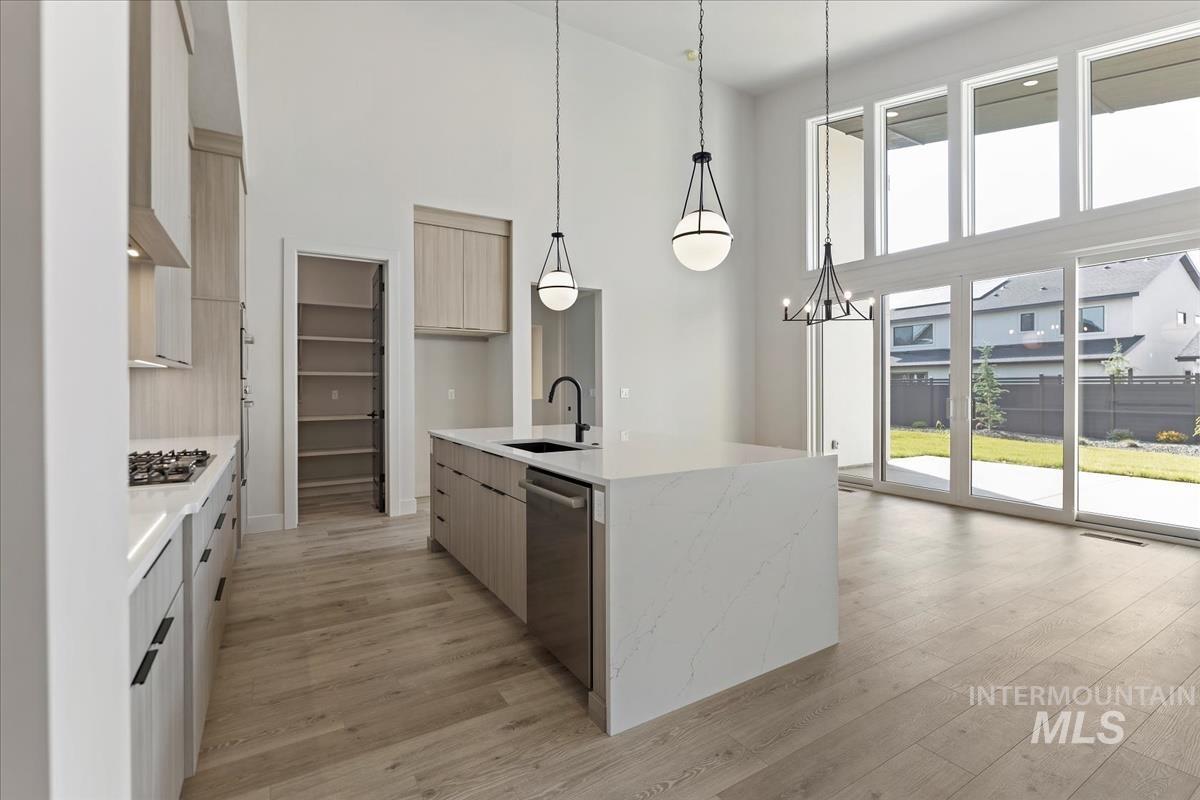 Kitchen featuring light stone counters, pendant lighting, a towering ceiling, modern cabinets, and an island with sink