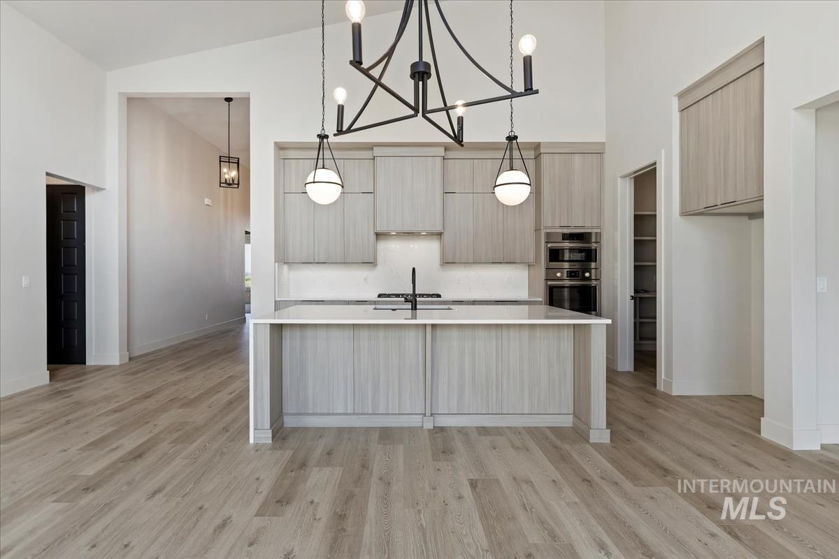 Kitchen with high vaulted ceiling, modern cabinets, pendant lighting, light wood finished floors, and a kitchen island with sink