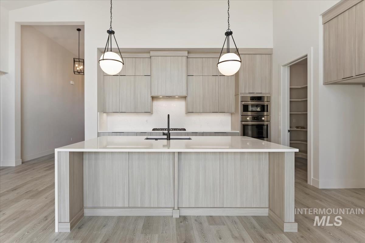 Kitchen featuring hanging light fixtures, light stone counters, light wood finished floors, and an island with sink
