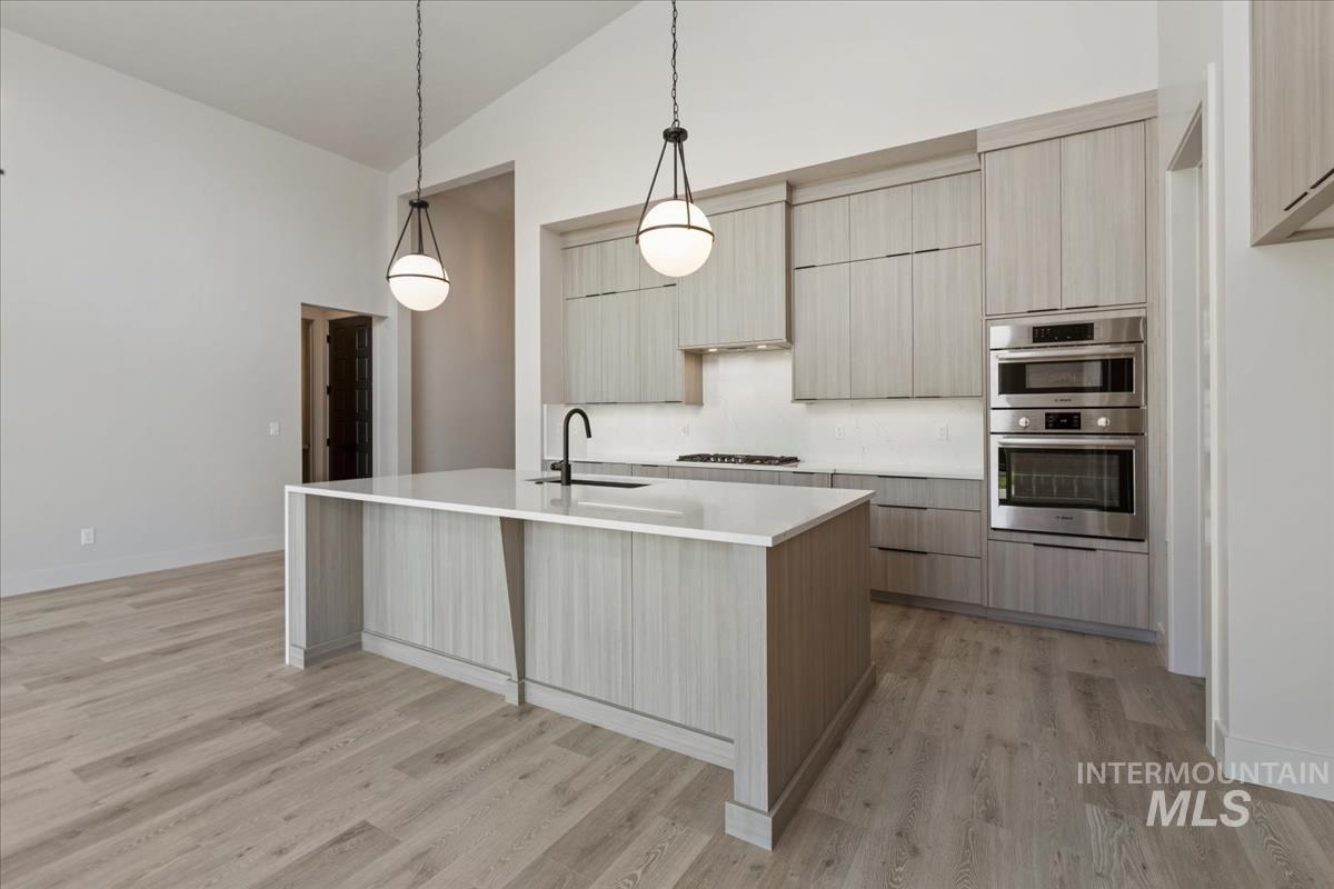 Kitchen featuring pendant lighting, modern cabinets, light wood-style floors, light stone countertops, and high vaulted ceiling